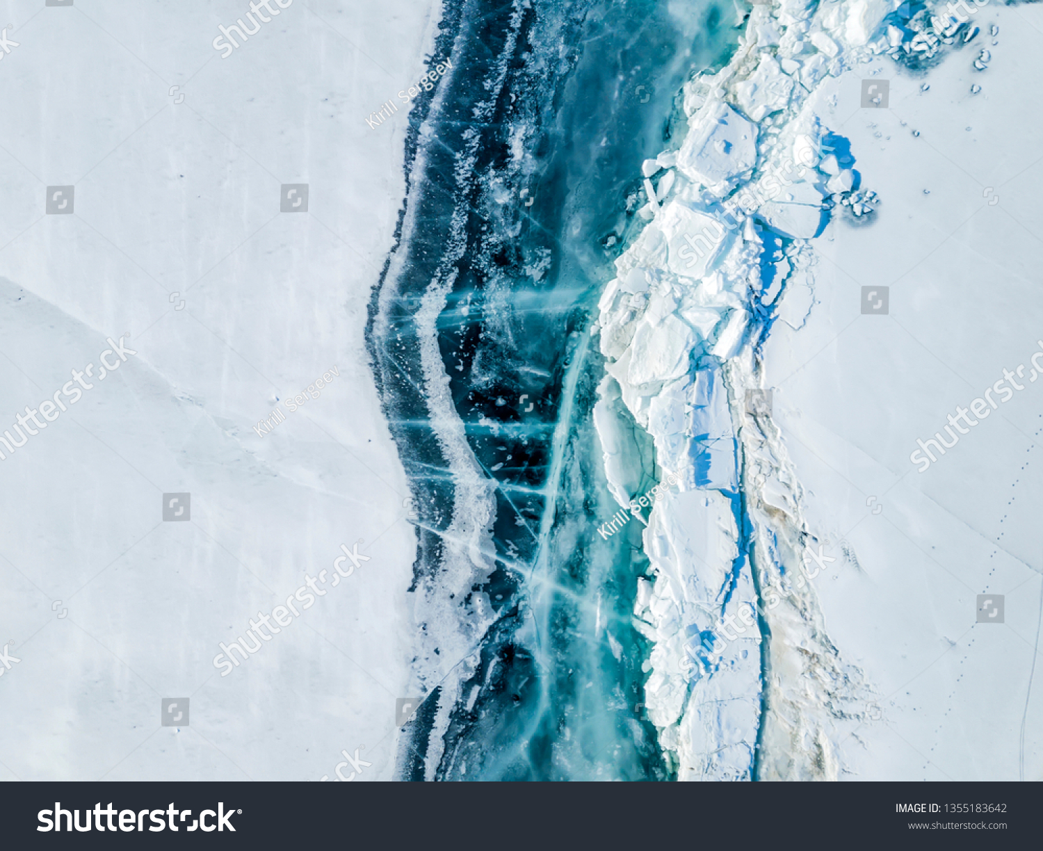 A large crack with bare ice and hummocks passes over the snow-covered surface of Lake Baikal in early spring. View from above. Siberia Russia