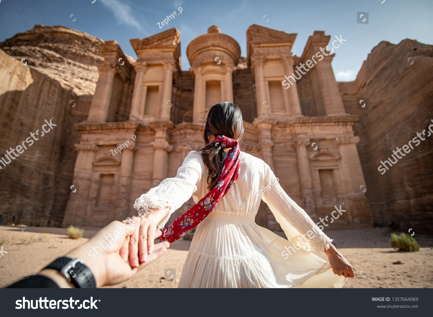Asian woman tourist in white dress holding her couple hand at Ad Deir or El Deir the monument carved out of rock in the ancient city of Petra Jordan. Travel UNESCO World Heritage Site in Middle East
