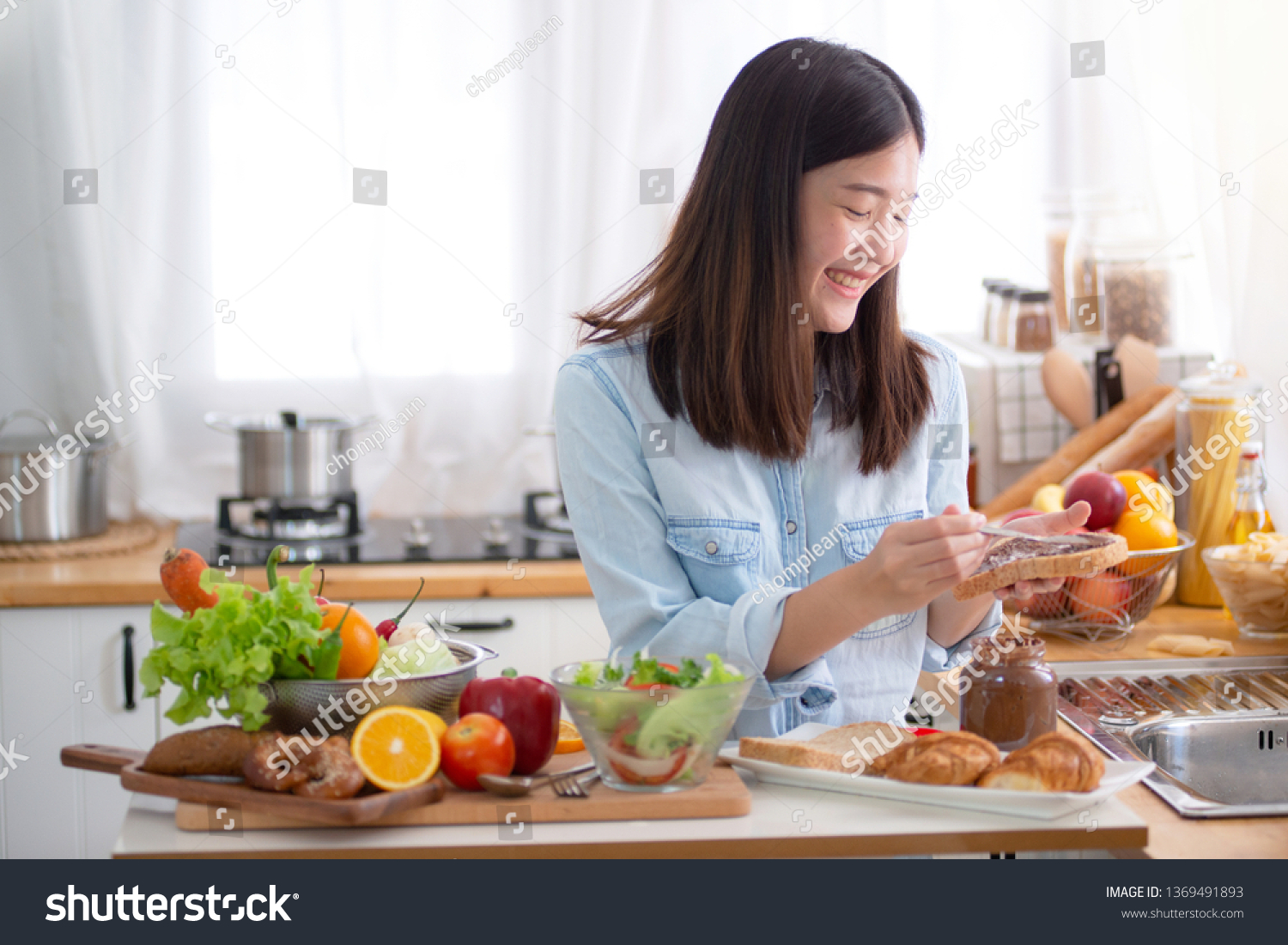 Young Asian woman apply jam on bread  and preparing a breakfast in the kitchen