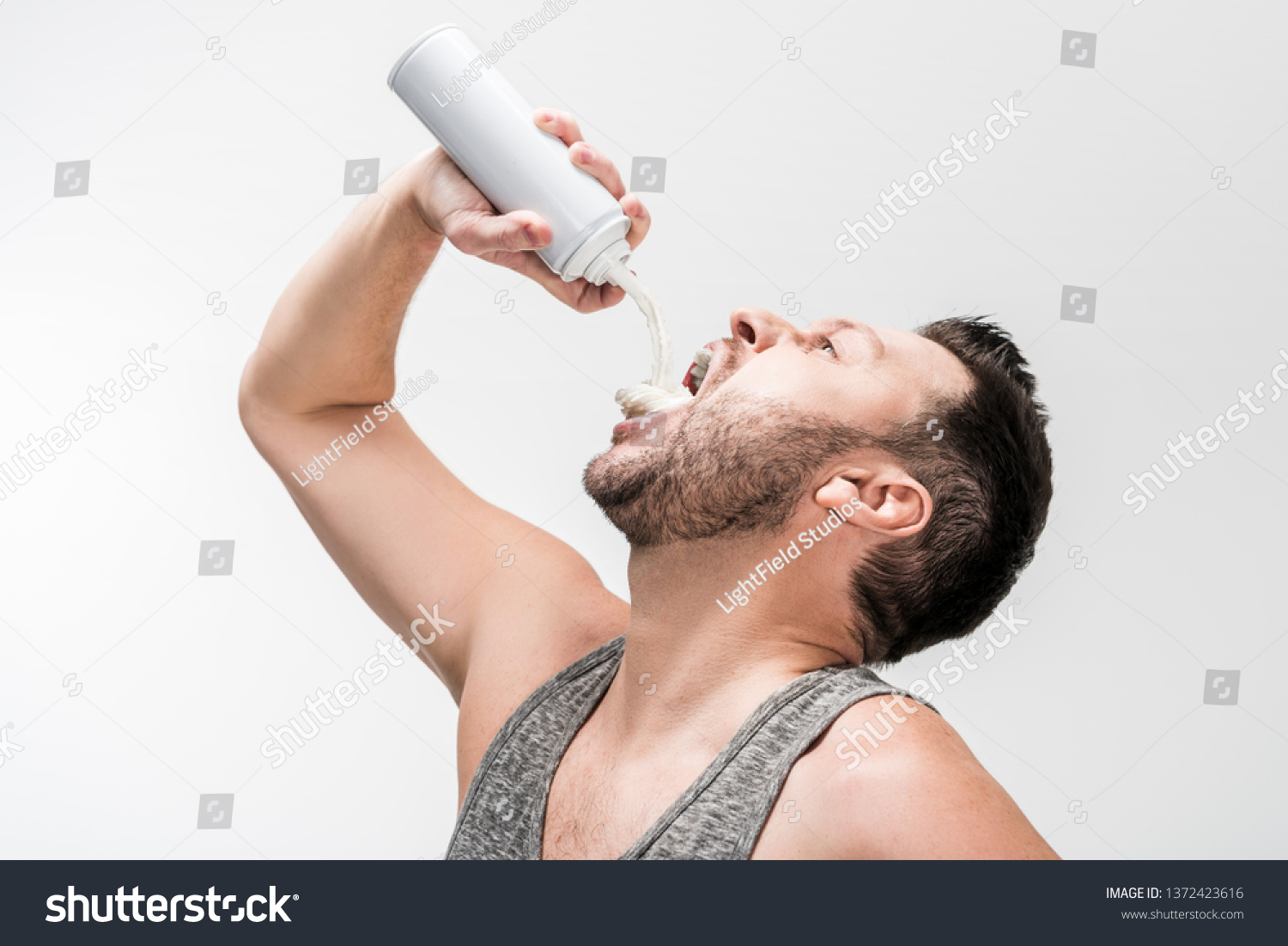 chubby man in tank top spraying whipped cream in mouth on white