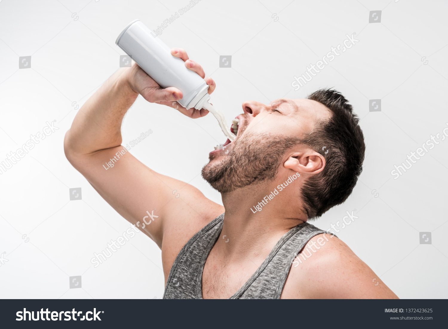 chubby man in grey tank top spraying whipped cream in mouth on white