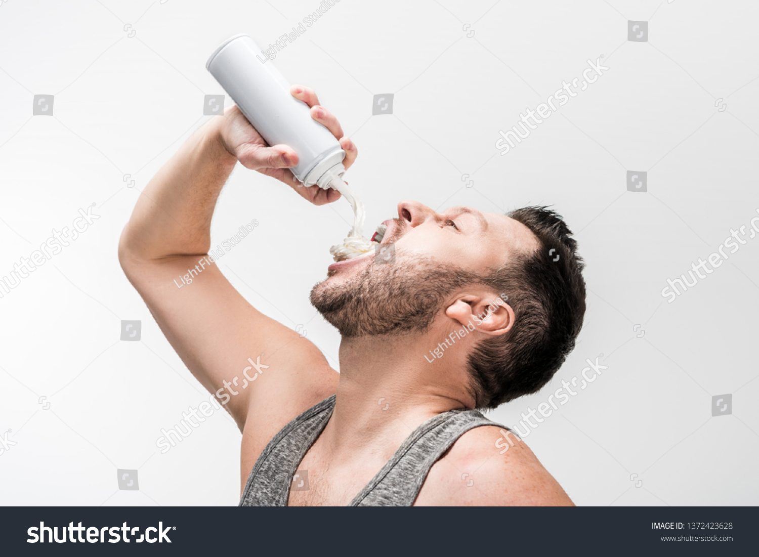 chubby man in grey tank top spraying whipped cream in mouth on white