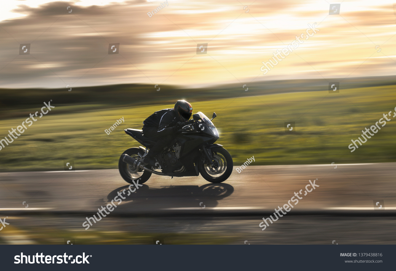 Man riding a sports motorbike at sunset  flying by with a field in the background.