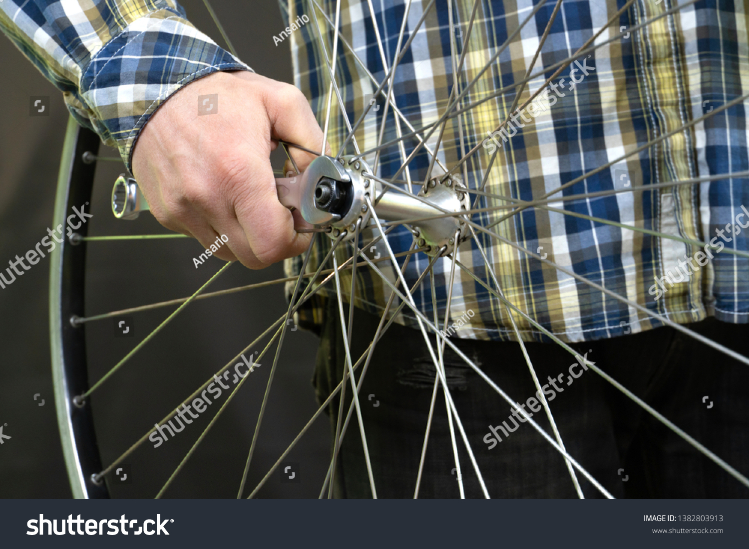 young trendy bike mechanic in a nice shirt repairs of the wheel