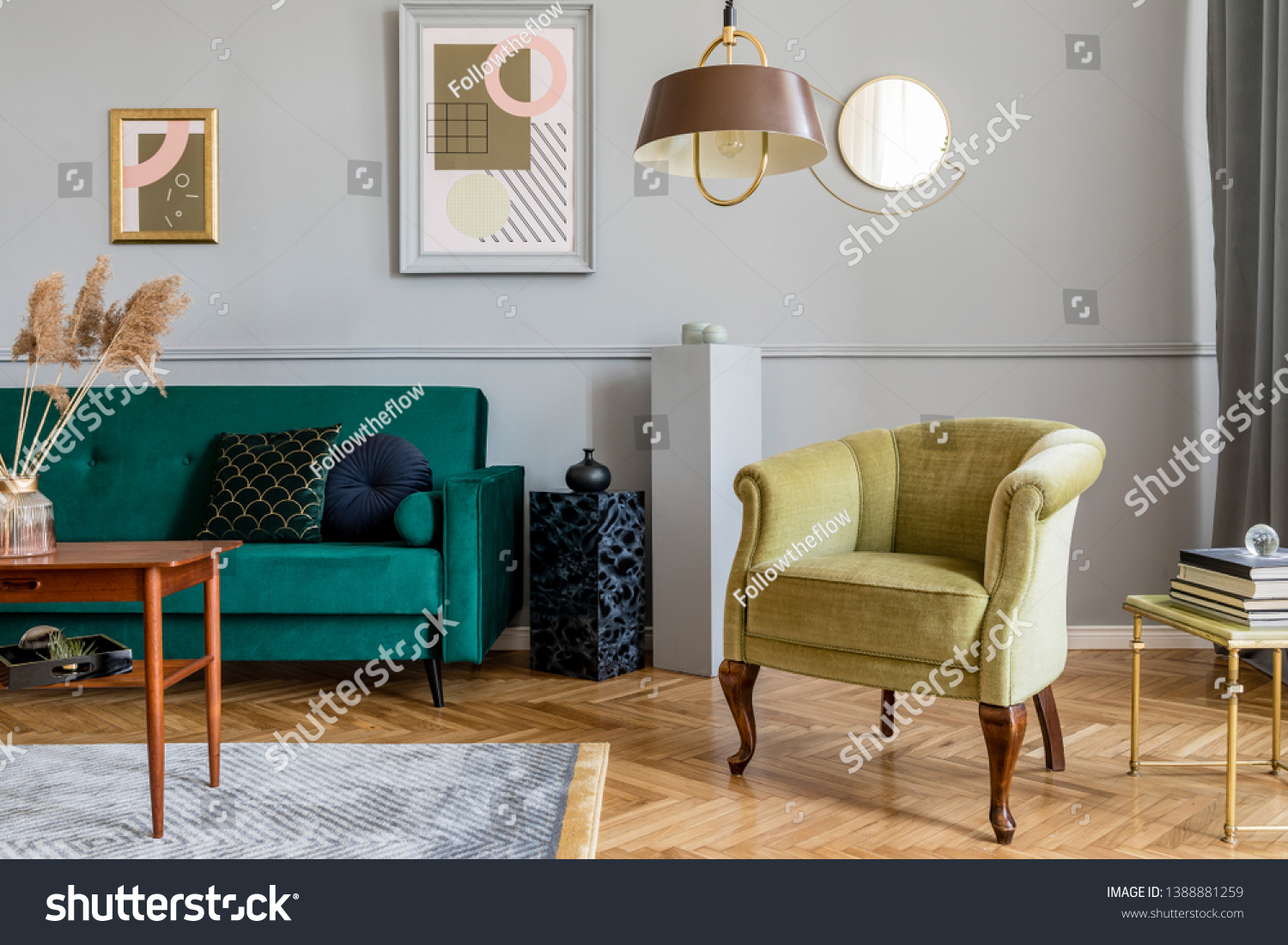 Stylish and tasty living room of apartment interior with elegant green velvet armchair and sofa brwon table design lamp and chic accessories. Abstract paintings on the gray wall. Luxury home decor.
