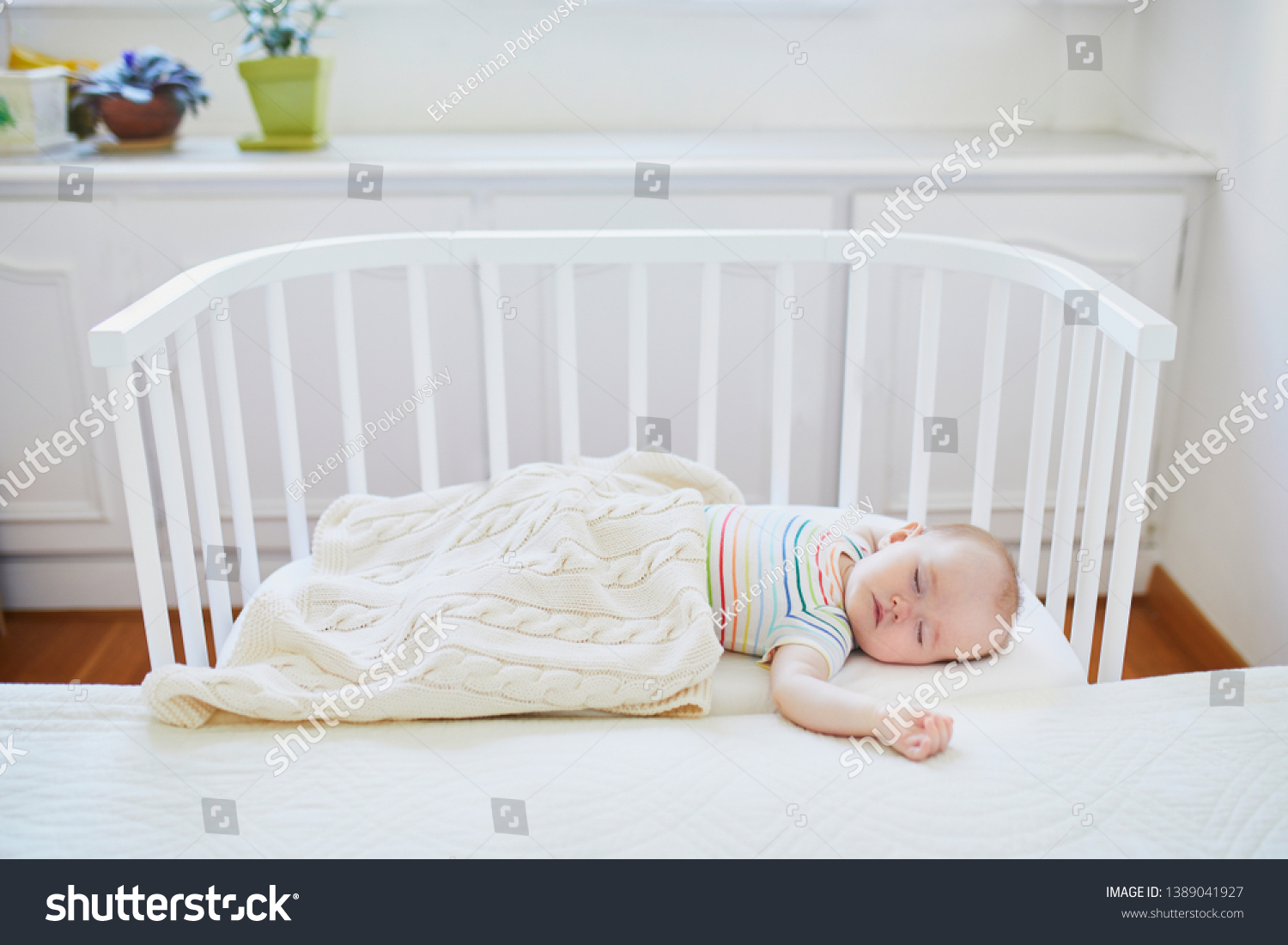 Adorable baby girl sleeping in cosleeper crib attached to parents' bed