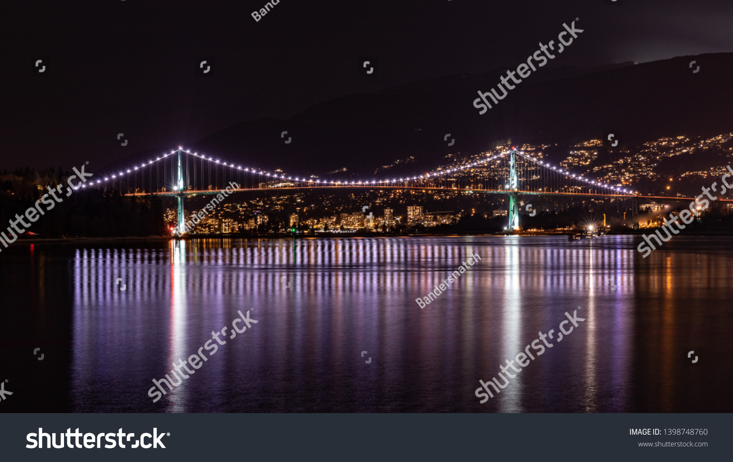 Night panorama of Lions Gate bridge connecting Stanley Park with North Vancouver BC Canada. Bridge lights reflecting on a silky water of Vancouver Harbor.