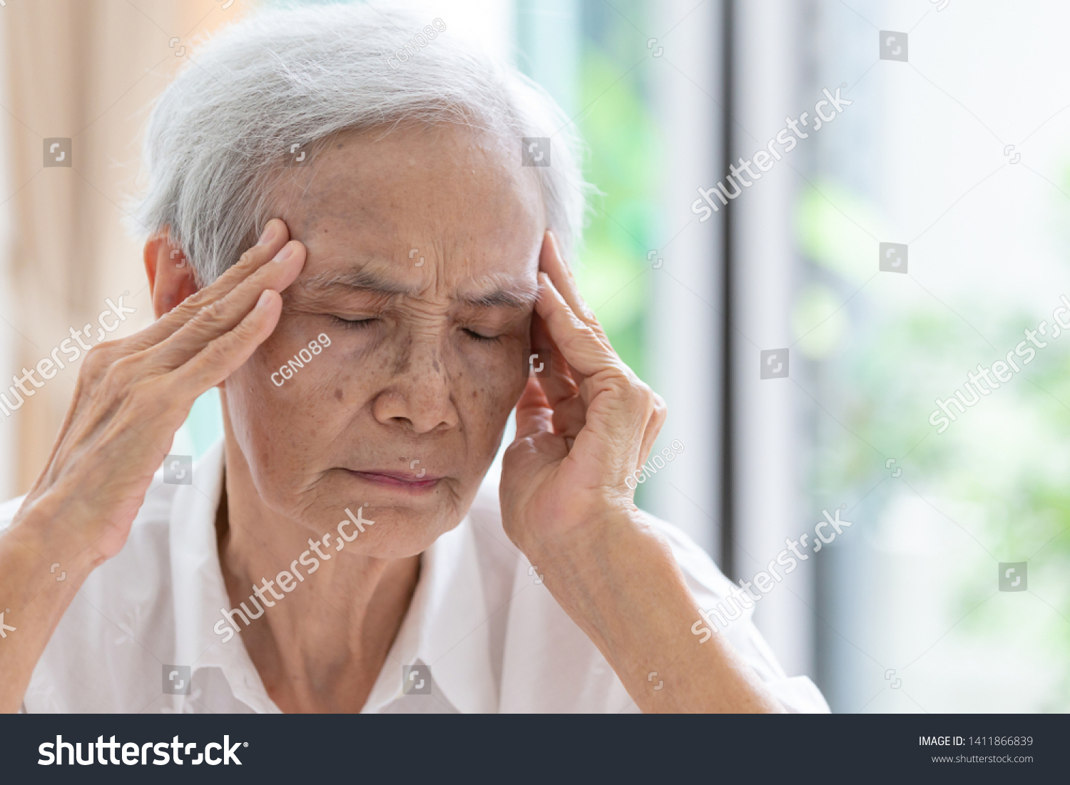 Asian senior woman has headache touching her head with her hands communicates the symptoms of vertigo;dizziness;migraine;sick depressed elderly people suffering from headache pain or memory loss