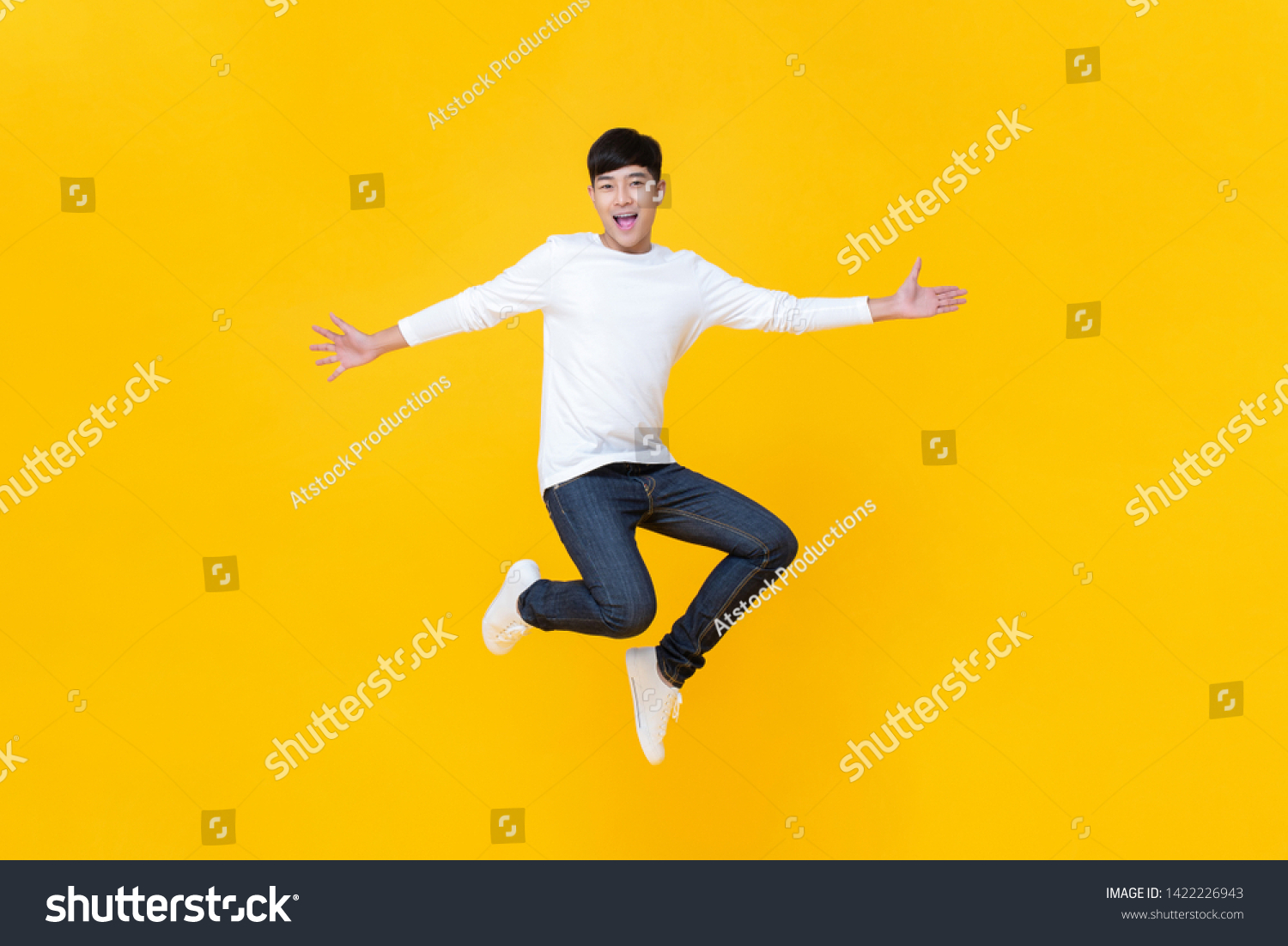 Young happy Korean teen jumping welcomely isolated on yellow studio background