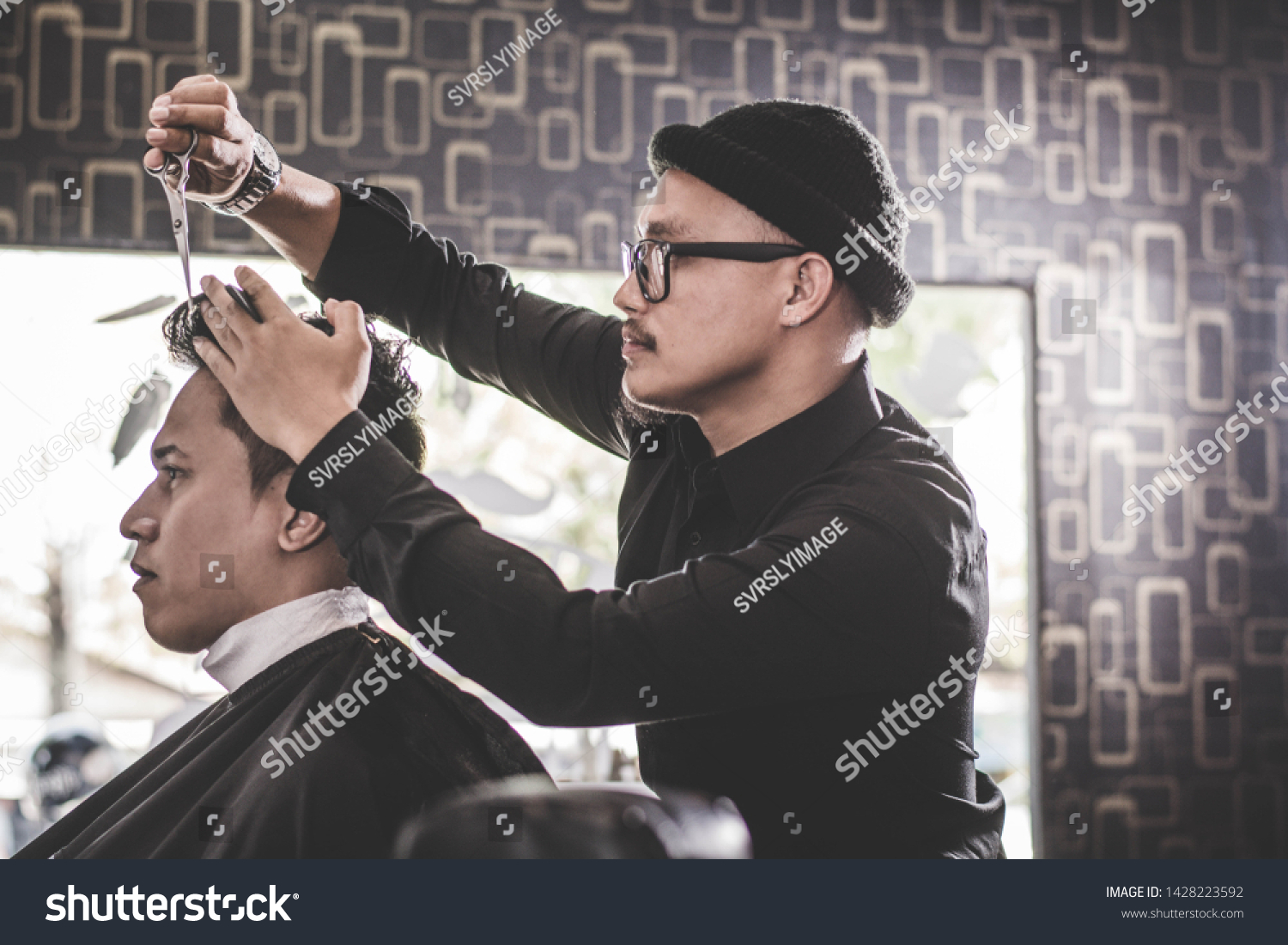 Portrait of professional barber making hair cut of his attractive man costumer with scissors and comb in vintage barbershop