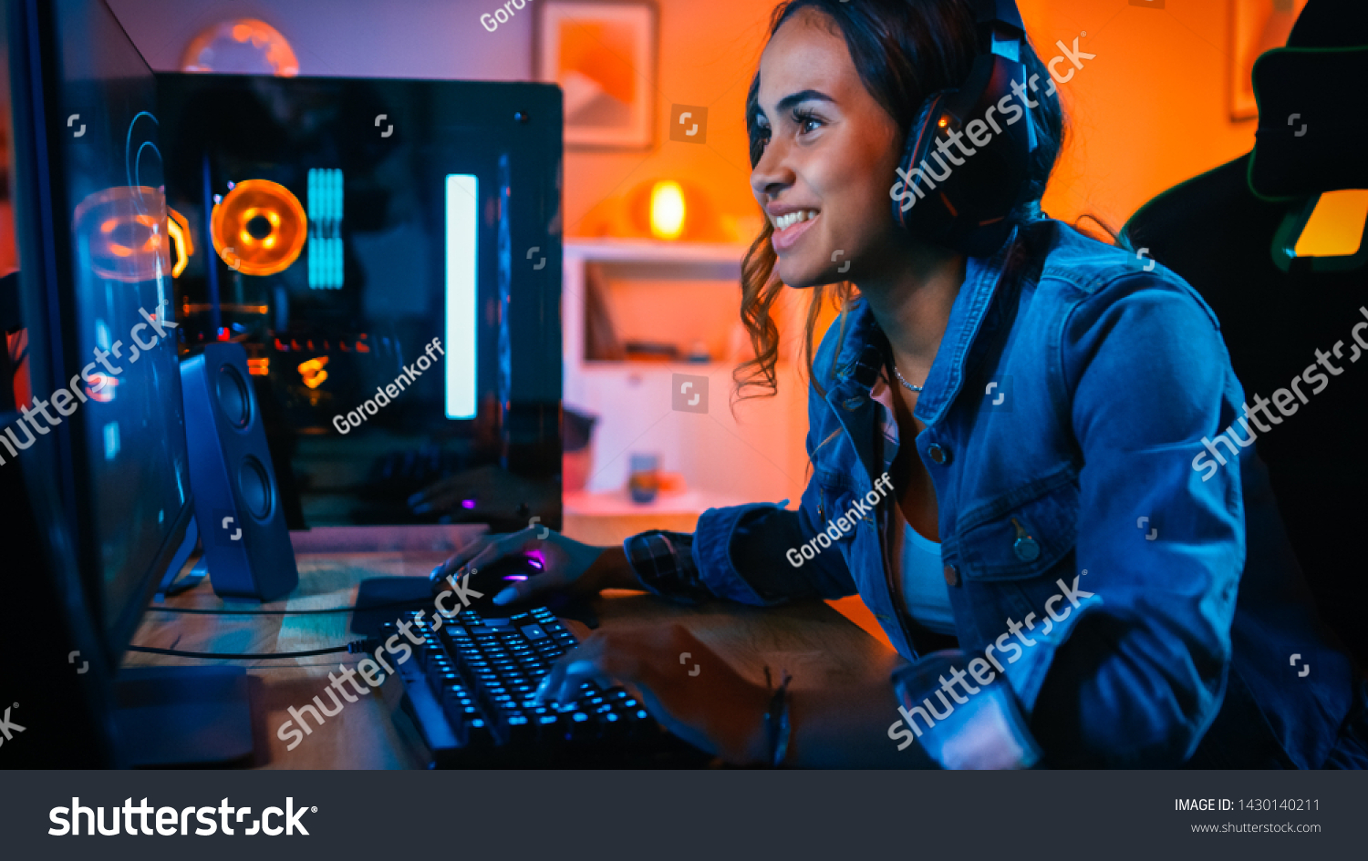 Pretty and Excited Black Gamer Girl in Headphones is Playing First-Person Shooter Online Video Game on Her Computer. Room and PC have Colorful Neon Led Lights. Cozy Evening at Home.