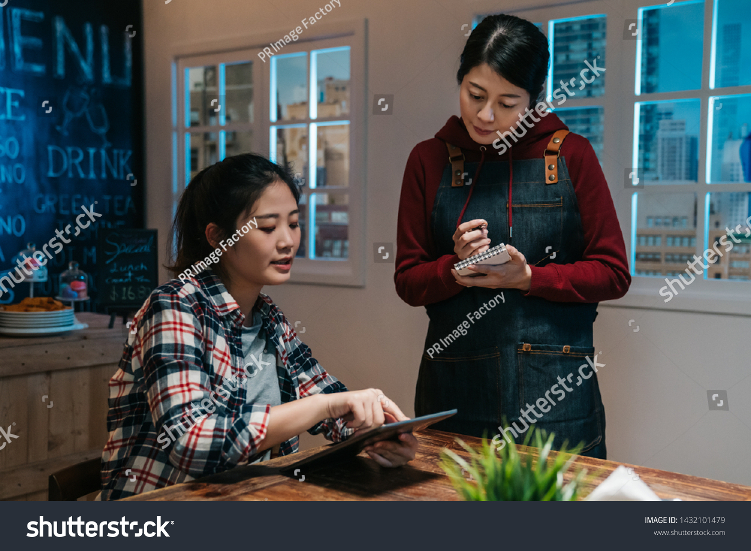 asian waitress takes order in restaurant using note and pen writing standing talking with client in night pub in modern city. cute girl customer point on digital tablet screen choose meal in bar.