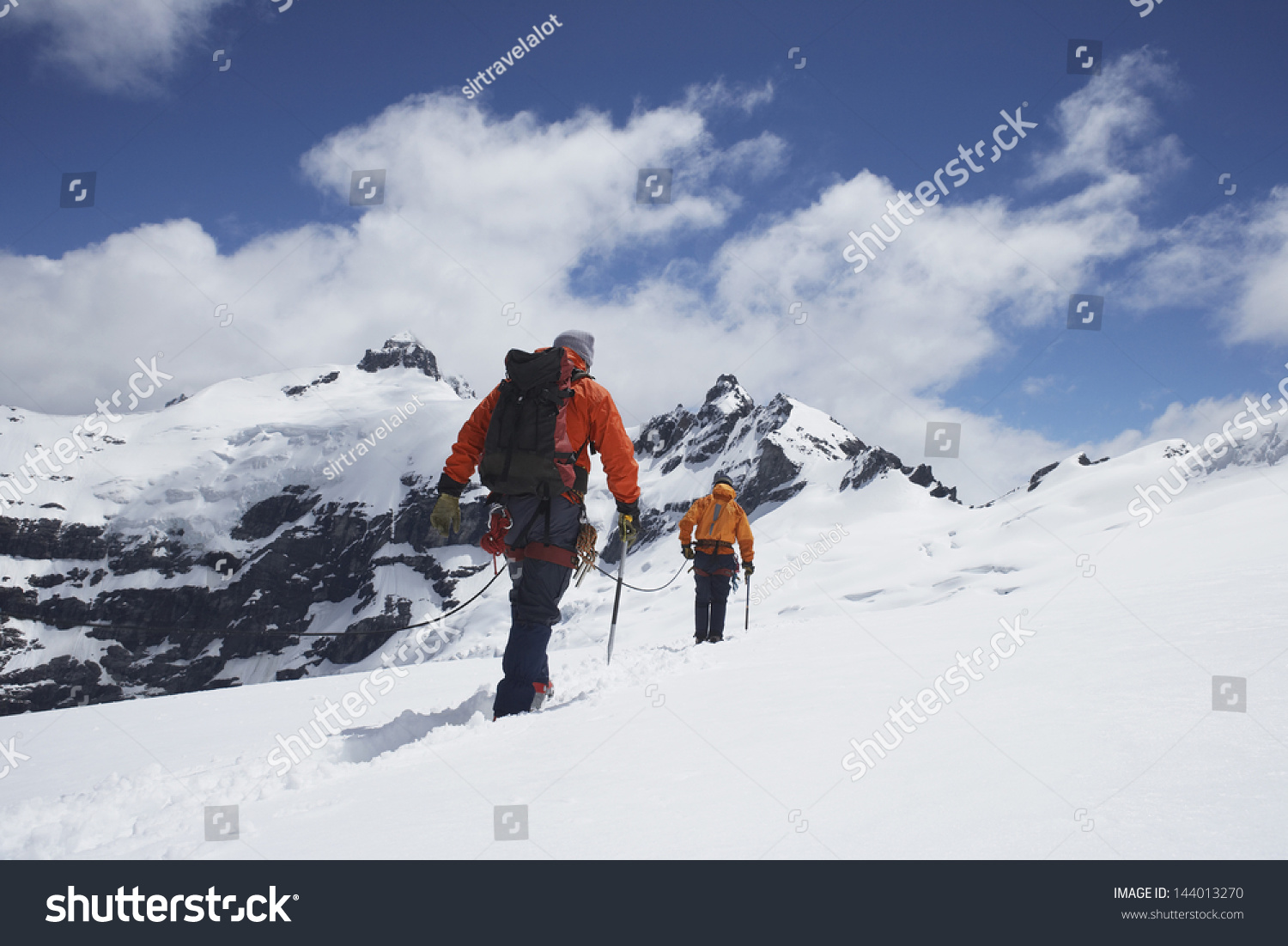 Rear view of two hikers joined by safety line in snowy mountains