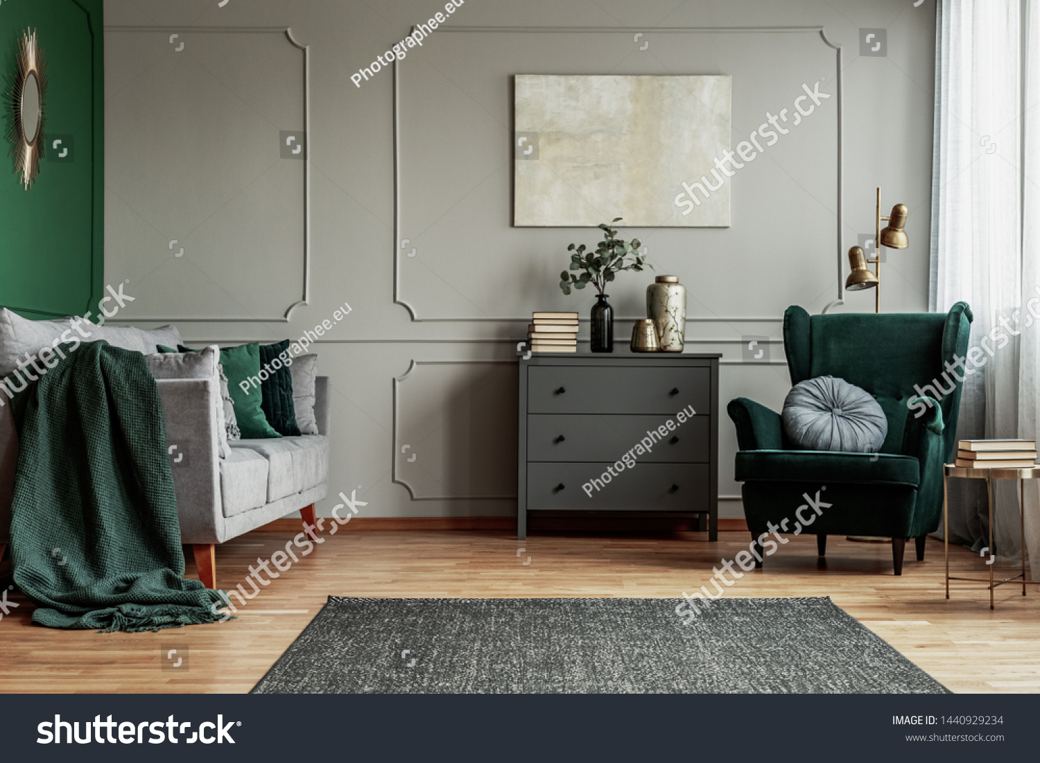 Abstract painting on grey wall o contemporary living room interior with emerald green armchair with round pillow commode and couch