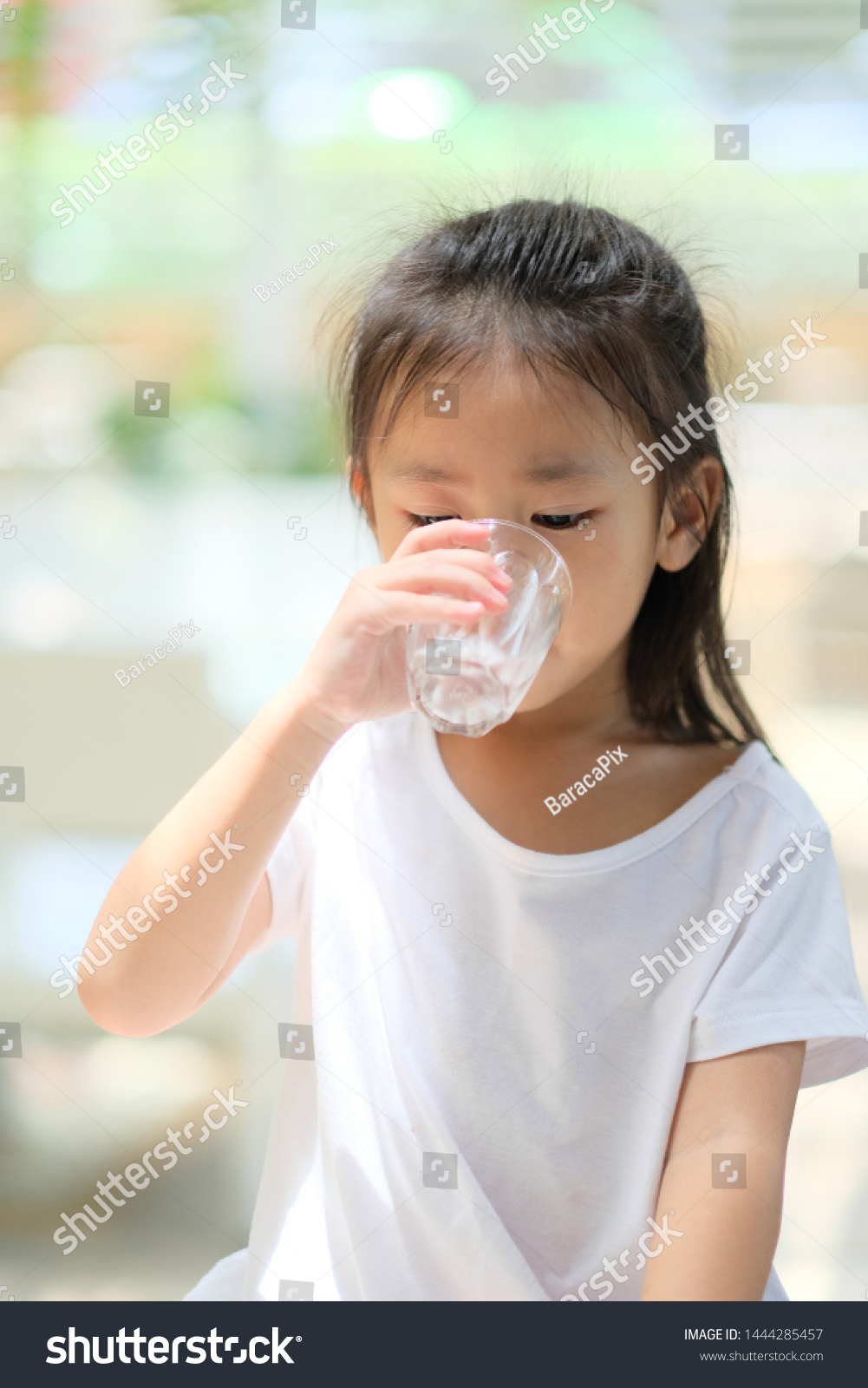 Close up Asian little girl with white shirt holding glass and drinking water