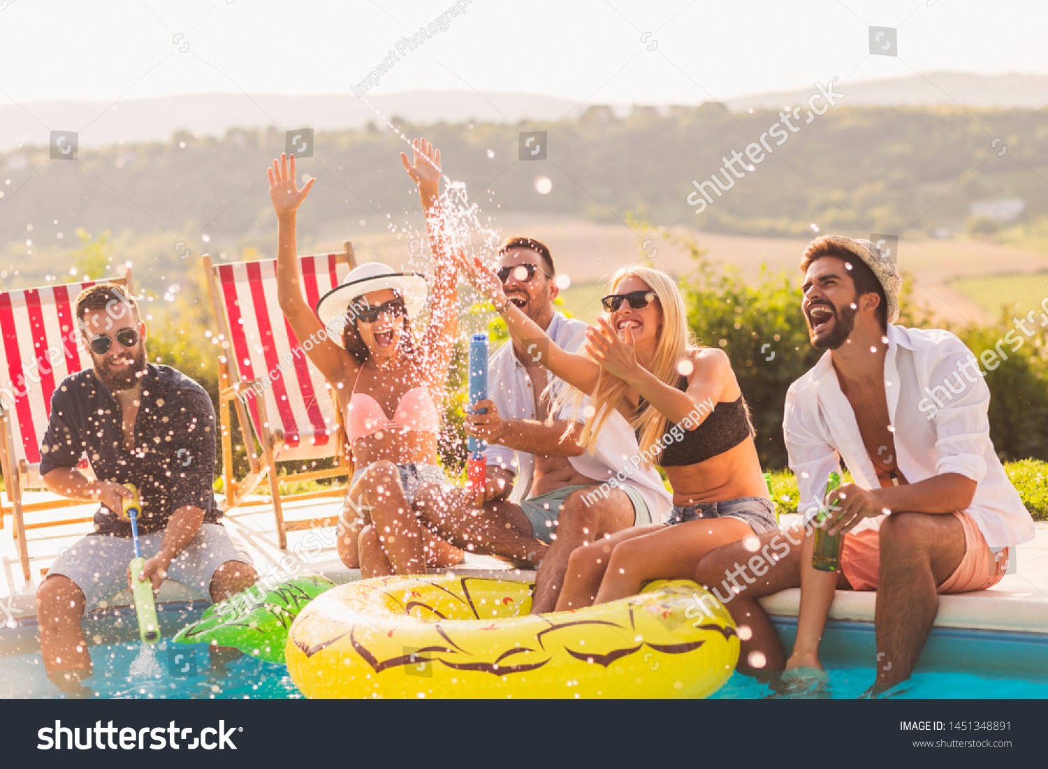 Group of friends at a poolside summer party sitting at the edge of a ...