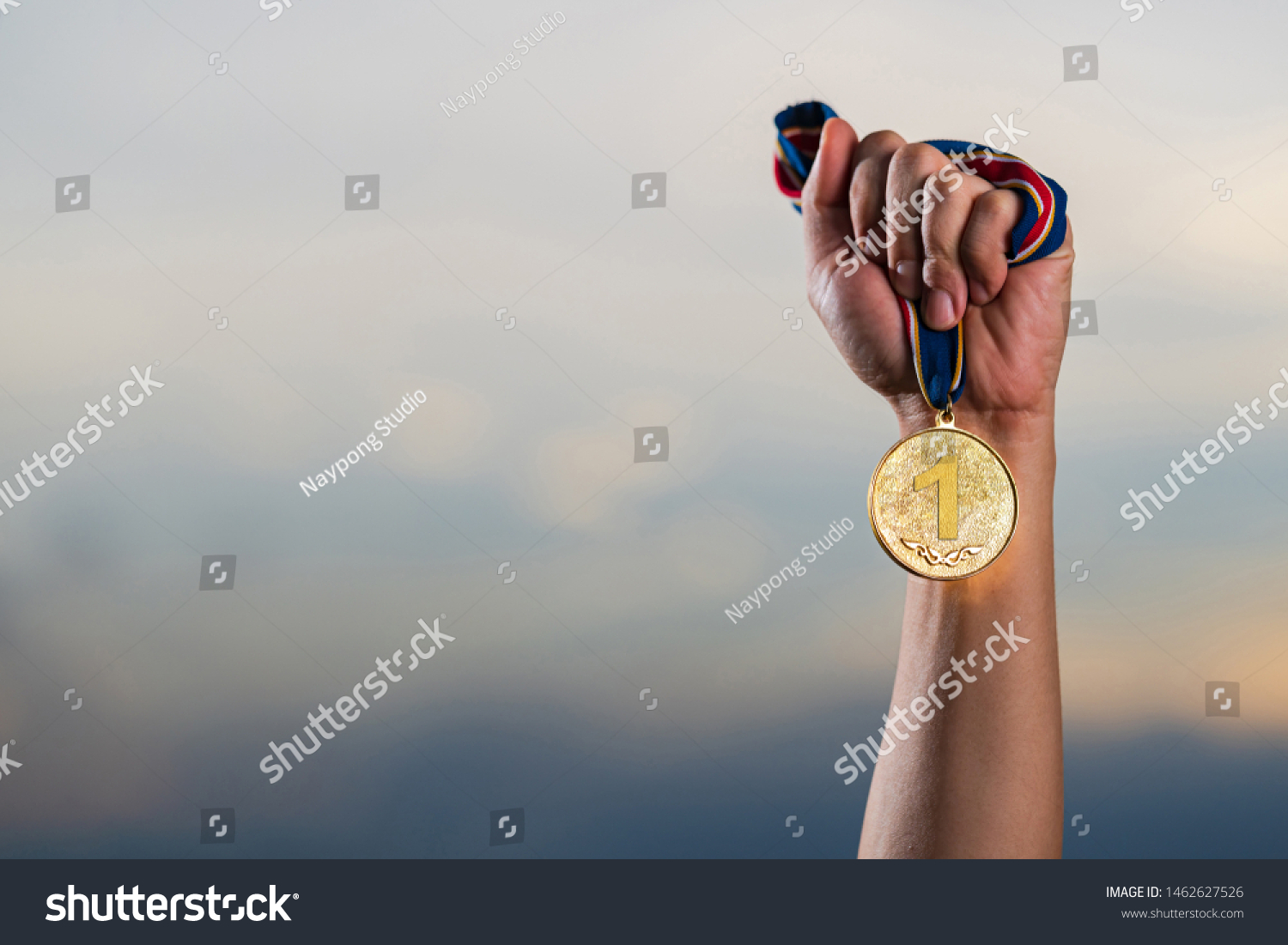 Hand holding gold medal on against cloudy twilight sky background  The winner and successful concept