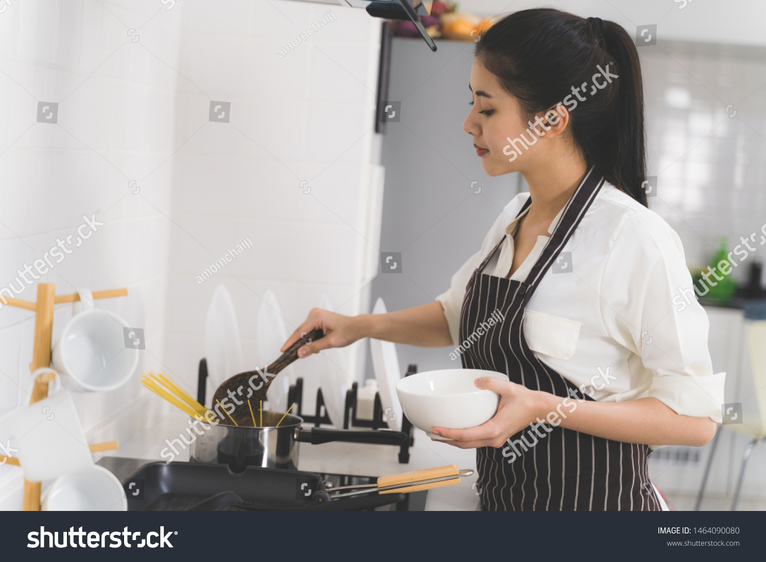 Beautiful asian woman or housewife is cooking food for family in white kitchen
