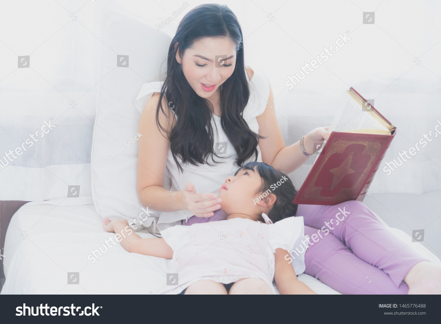Happy mother and daughtermother reading a book to her daughterin bed together to enhance child development and learning to read relaxing in bedroom enjoy bedtime stories