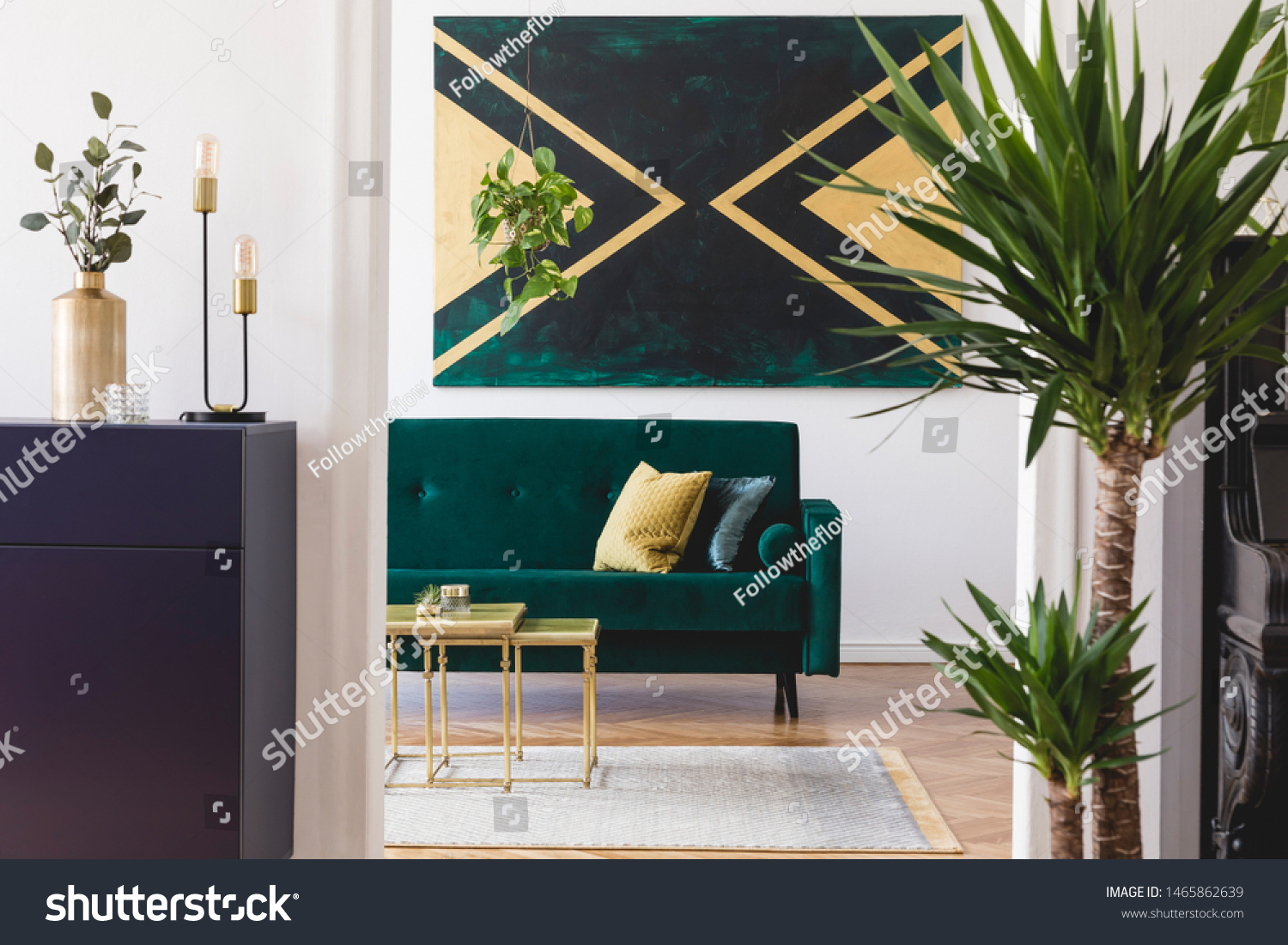 Modern and luxury interior of living room with pomegranate shelf gold coffee table velvet sofa tropical plant and elegant accessories. Design paintings on the wall. Stylish home decor. Template