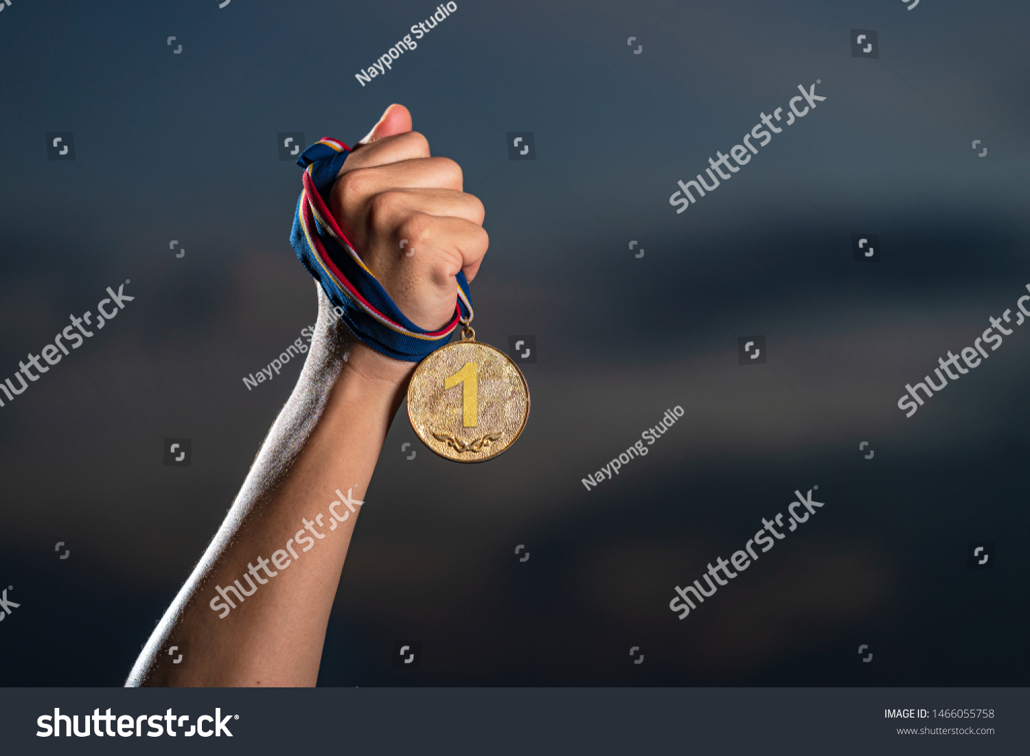 Hand holding gold medal on against cloudy twilight sky background  The winner and successful concept
