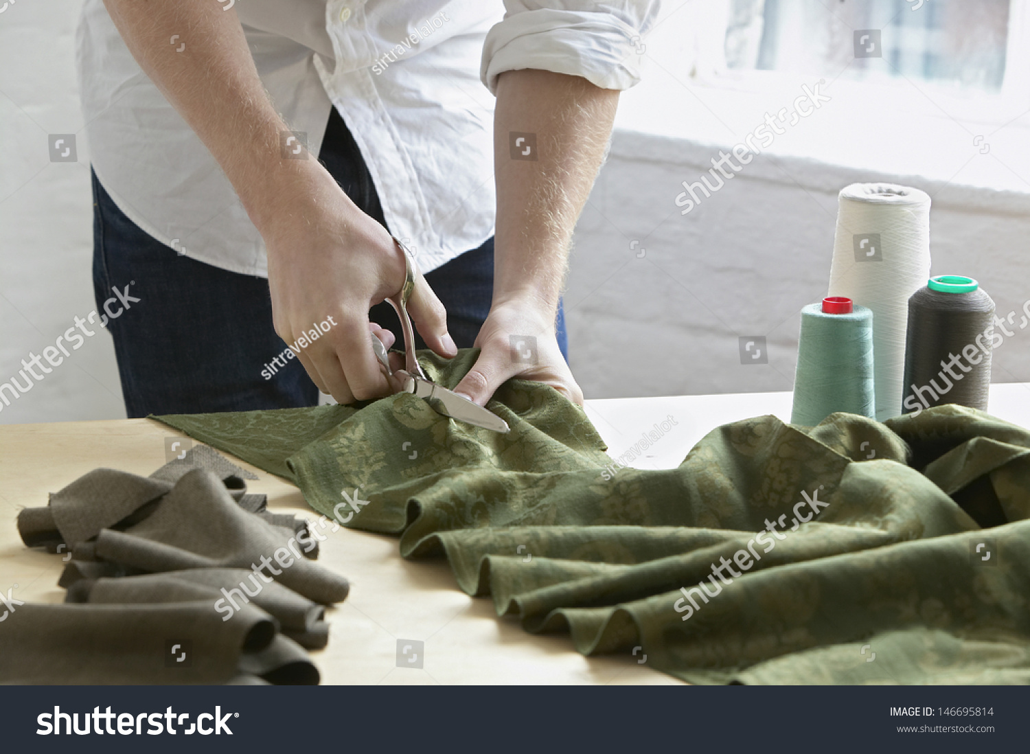 Midsection of young male tailor cutting piece of cloth at table in fashion studio