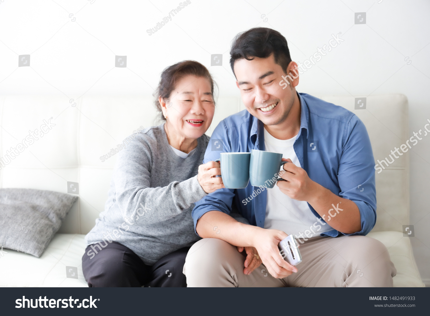 Asian senior grand mother and son in blue shirt drinking coffee and talking happy and smile face in living room