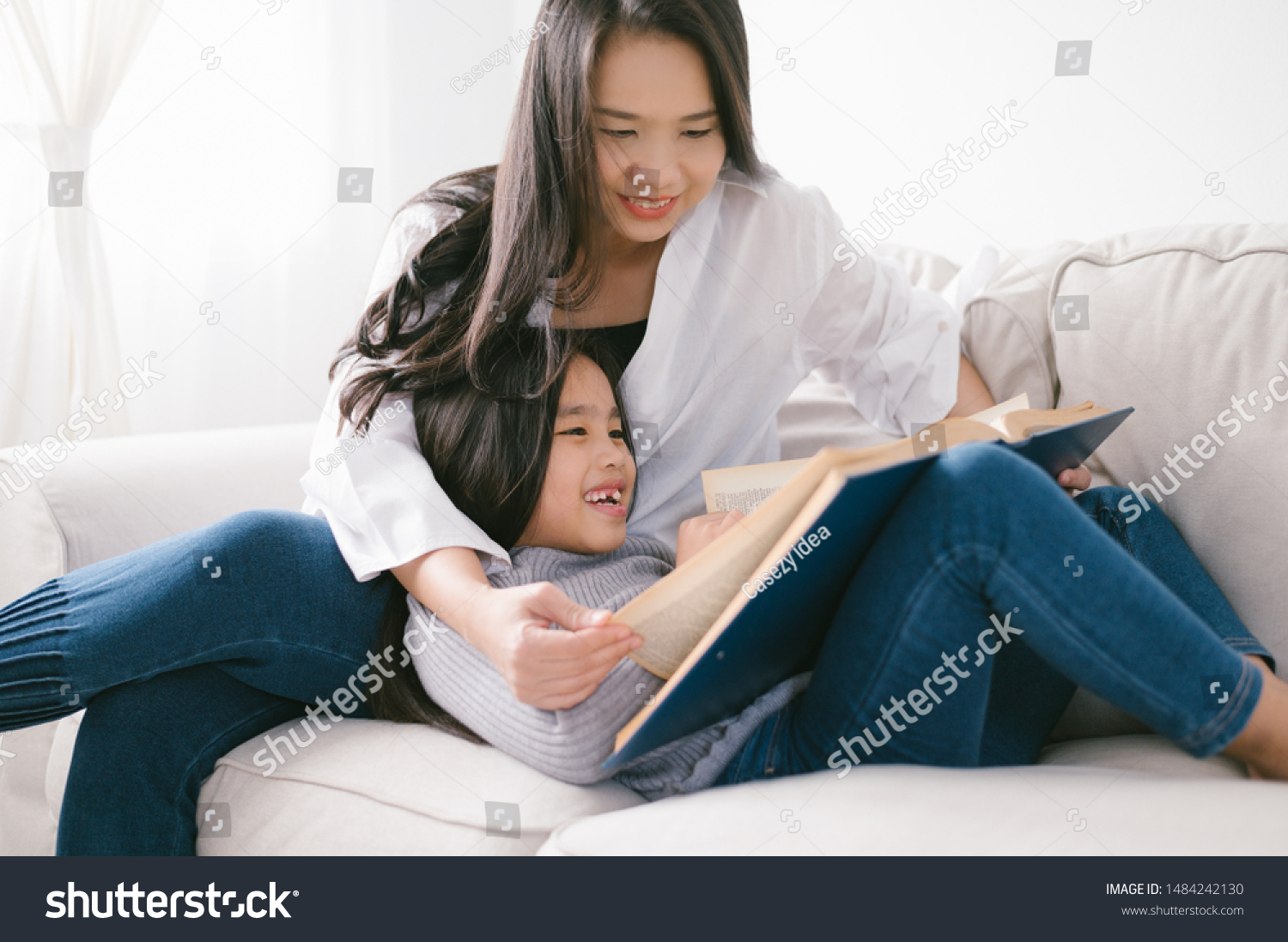 happy child little asian girl reading a books on the table in the living room at home. family activity concept