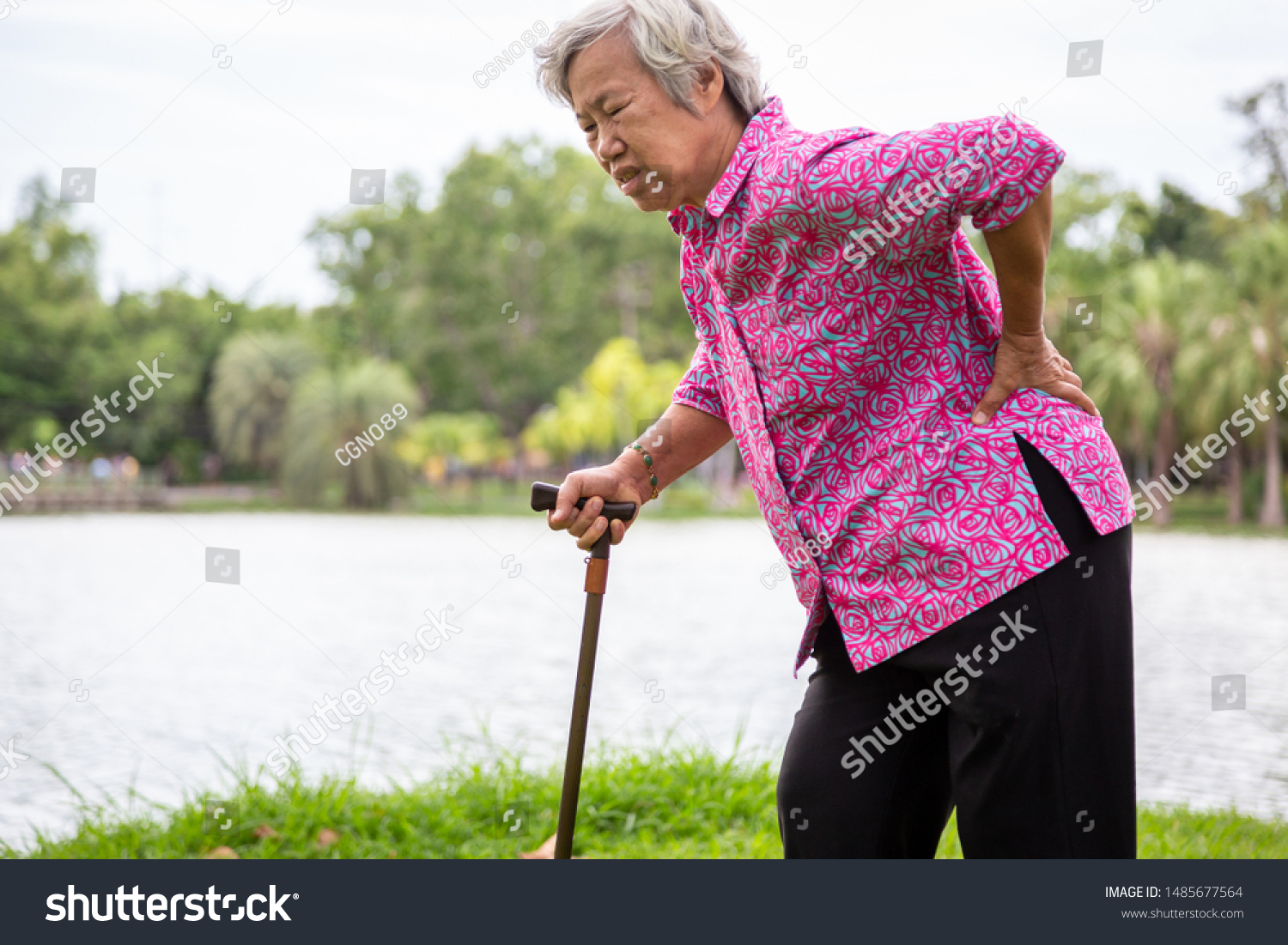 Asian senior woman with hip joint pain while walking female patient having backache lumbago pain hands touching on the hip in outdoor park elderly people suffering from ribbing pain or waist pain