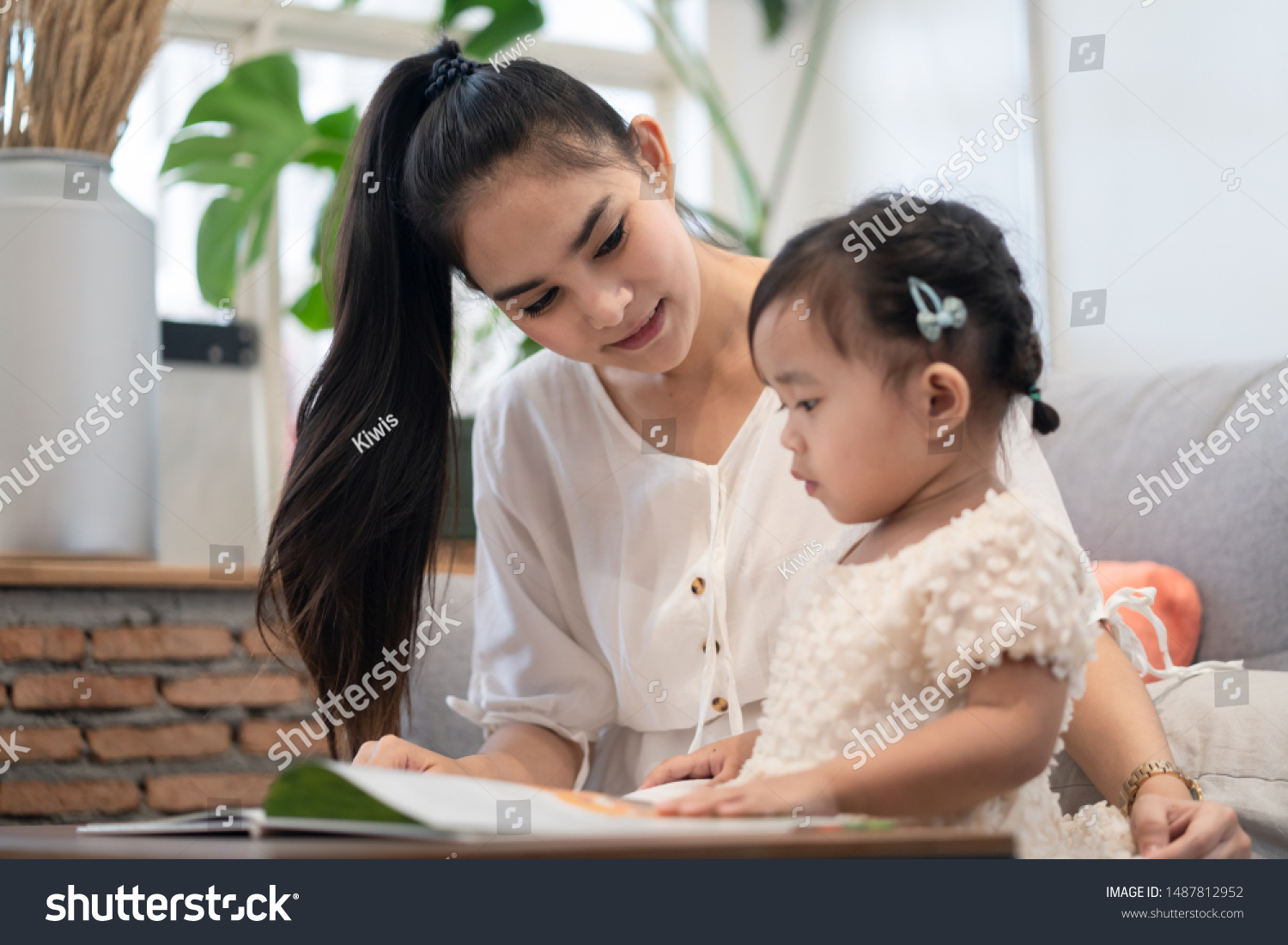 Asian pretty young mother and her daughter reading tale story book together. The mom looking the little girl with happiness. Good relationship of mom and kid. Family activity and education concept.