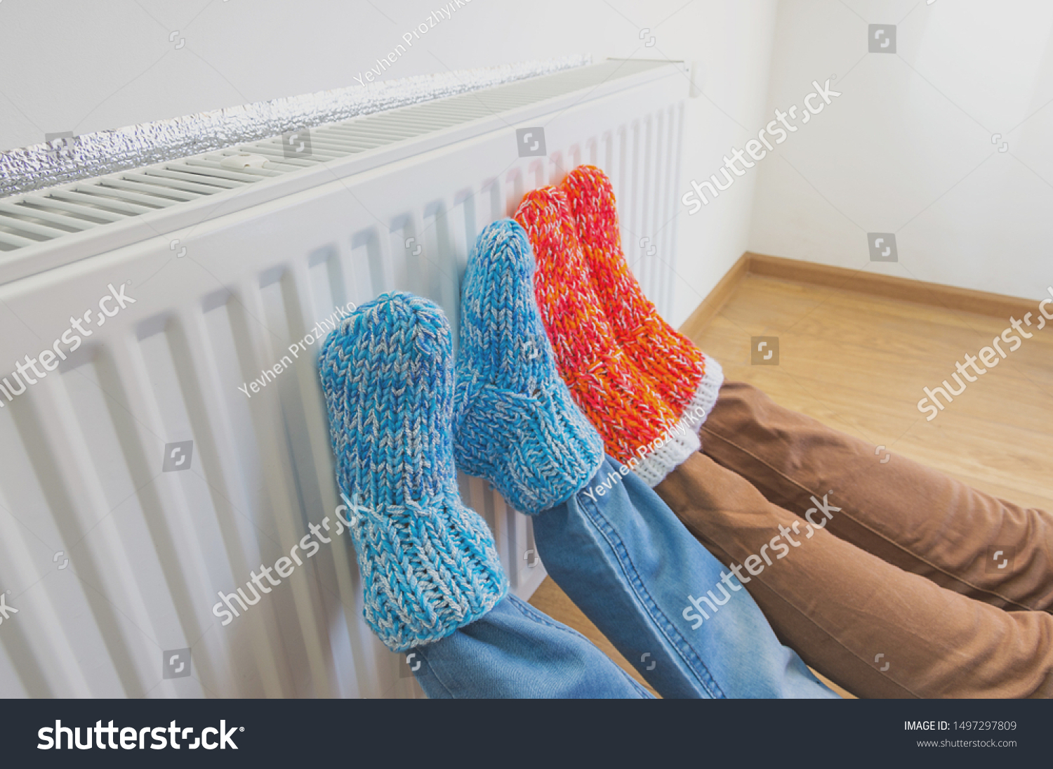 Family in warm knitted woolen socks near a home heater in cold winter time. The symbolic image of the heating season at home. Part of body selective focus.