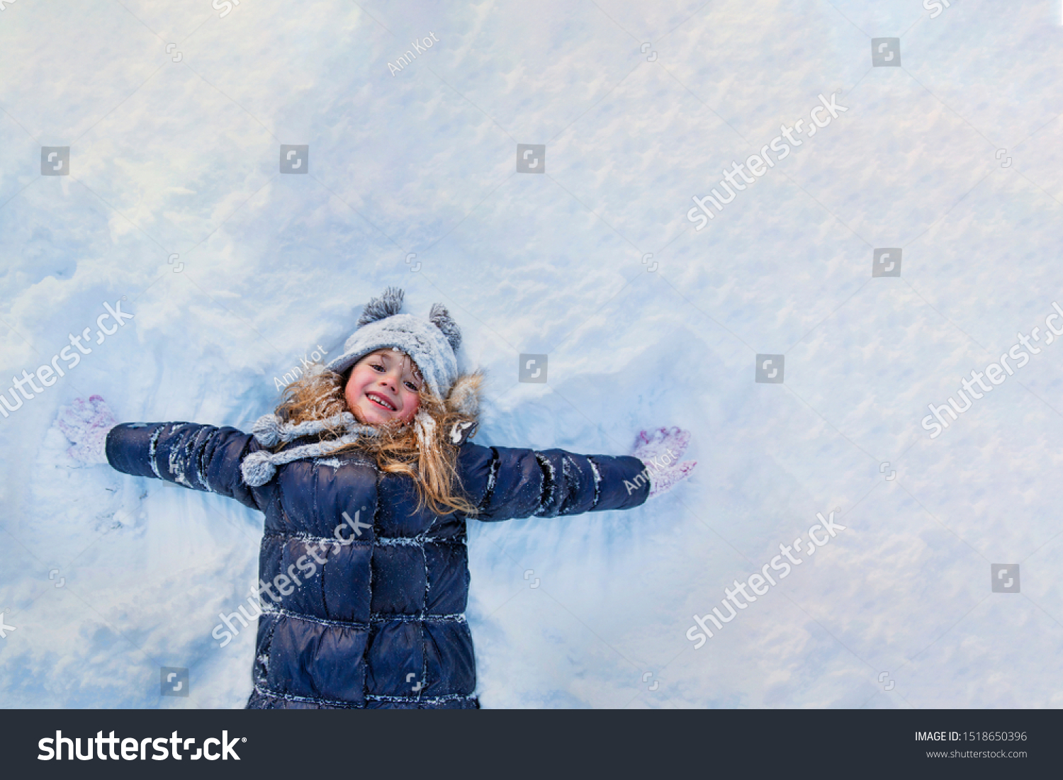 Beautiful little girl wearing navy jacket and knitted hat playing in a snowy winter park. Child playing with snow in winter. Kid play and jump in snowy forest. Family vacation with child in mountains