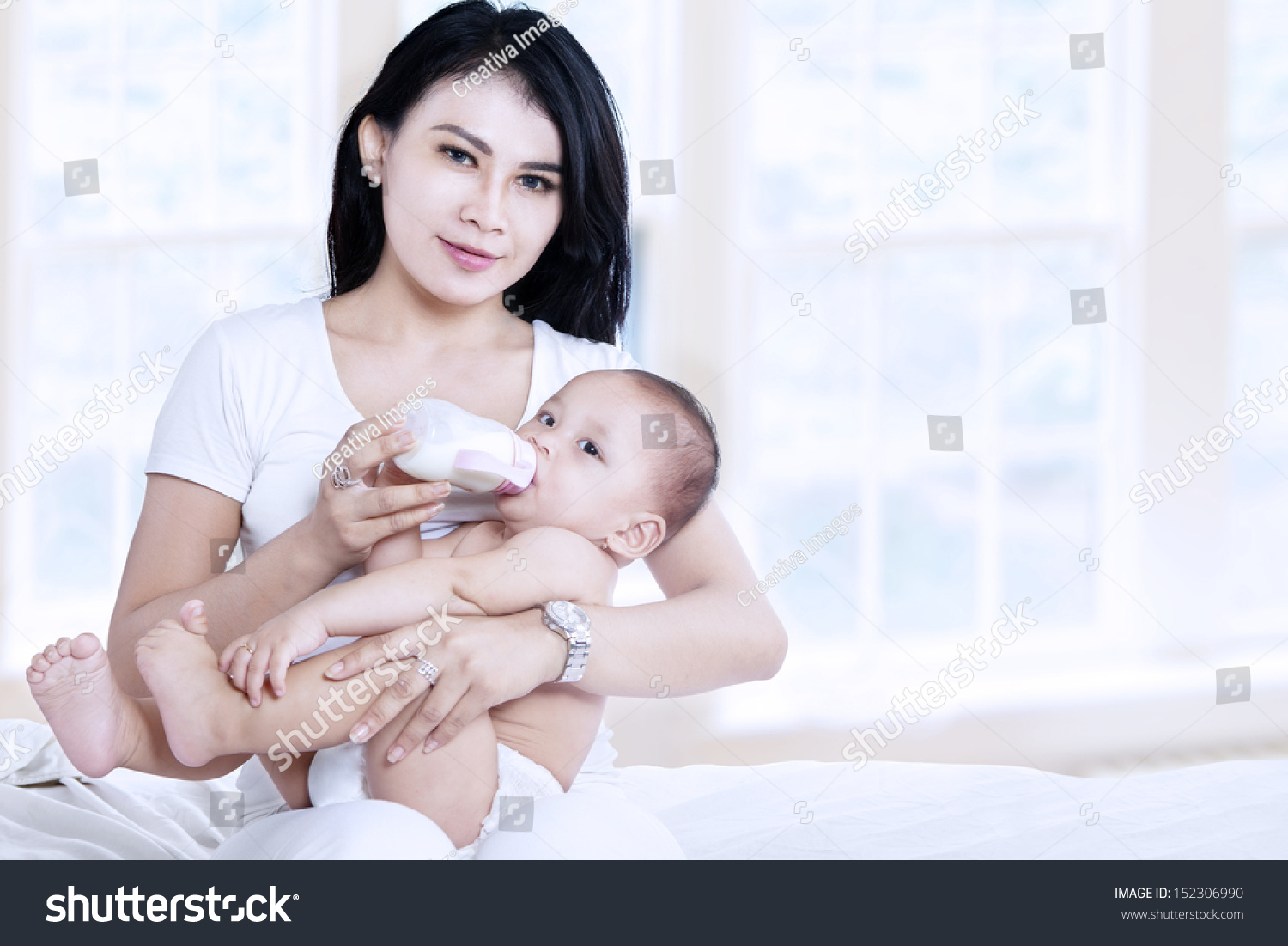 Asian mother feeding her baby with milk at home