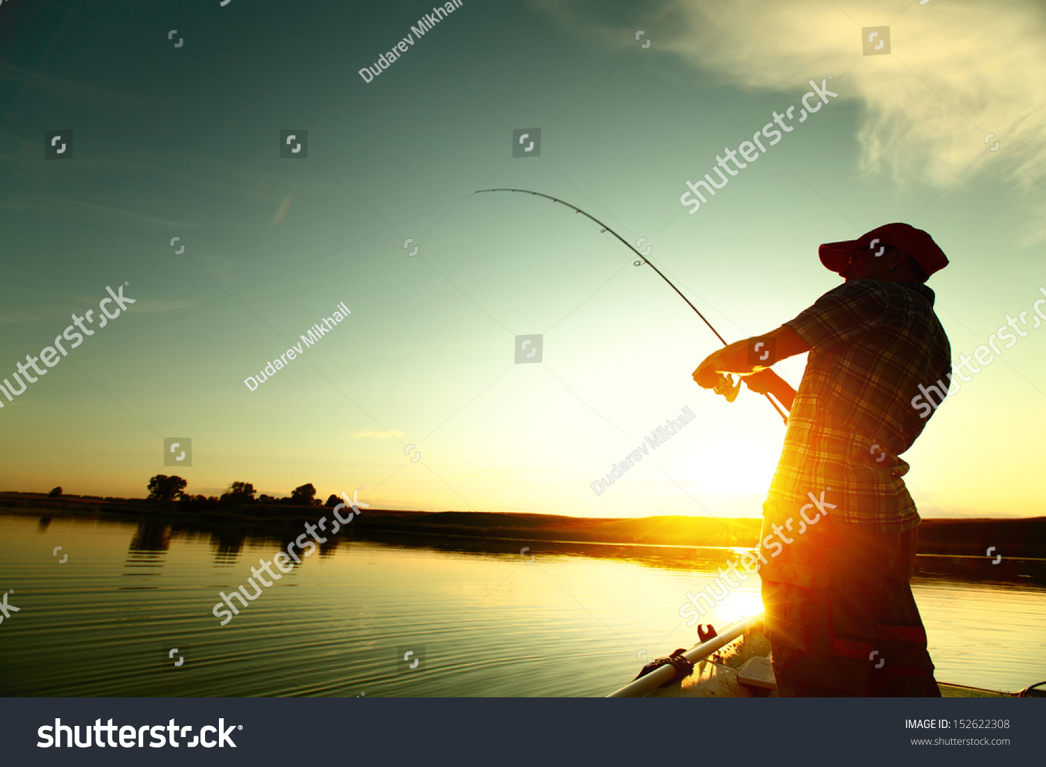 Young man fishing on a lake from the boat at sunset