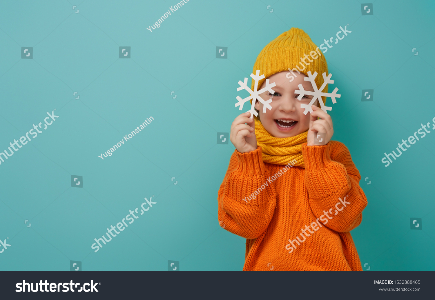 Winter portrait of happy child wearing knitted hat snood and sweater. Girl having fun playing and laughing on teal background. Fashion concept.