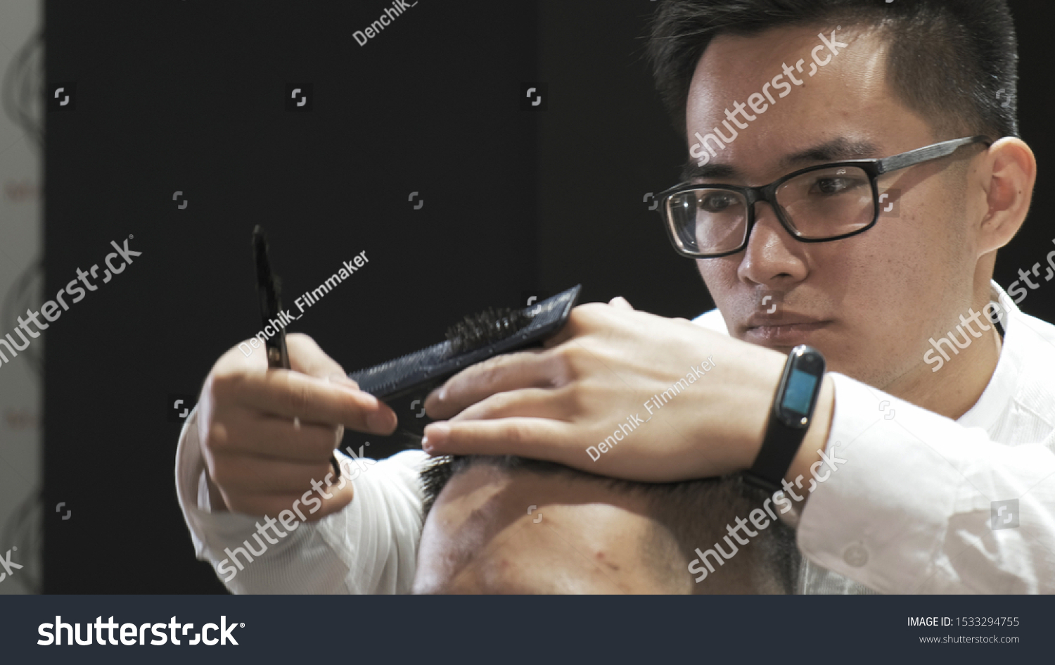 Close-up Asian hairdresser with glasses combing and cutting hair to client in salon. Creates a modern hairstyle