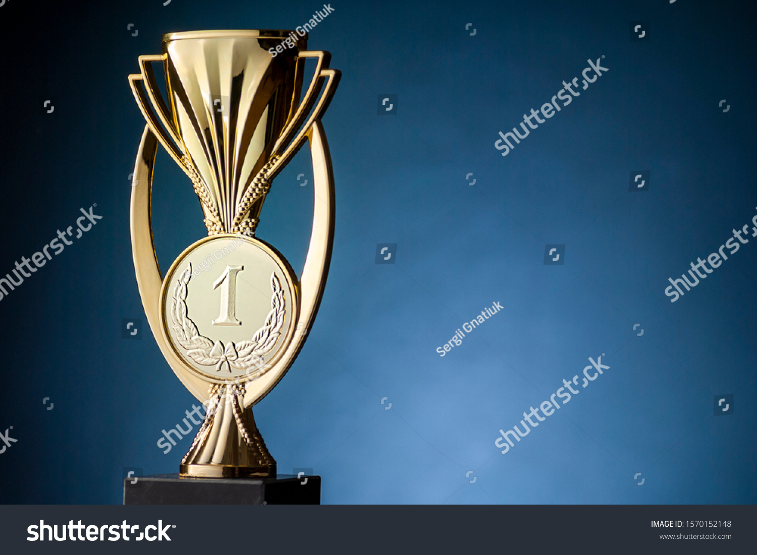 Gold championship winners trophy or cup placed to the side on a blue background with copy space
