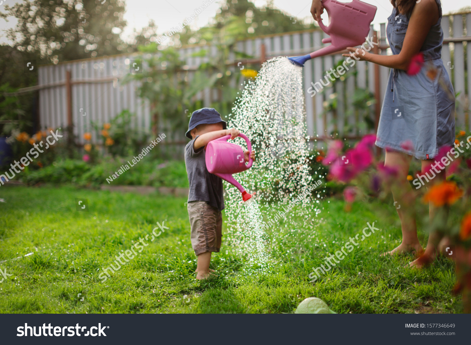 Mom and boy child water the garden together Mom’s little gardener assistant taking care of children and garden. Mother watering her son from watering can take care of trees and plants wet child