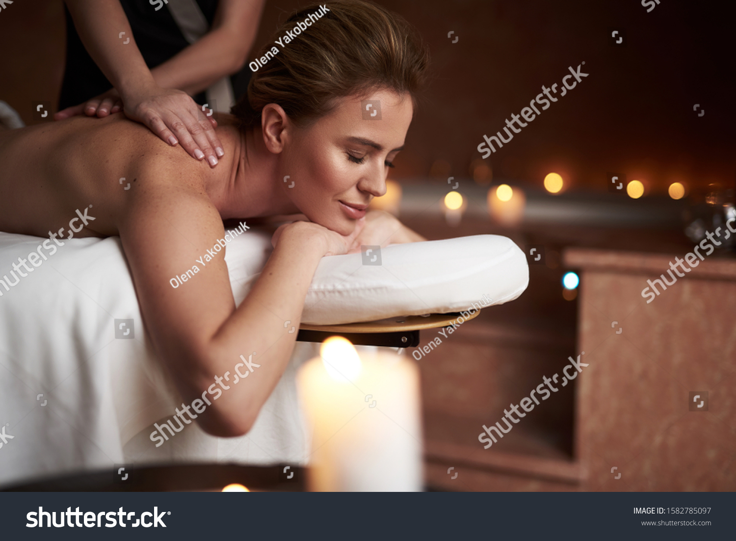 Concept of relaxation and body care. Close up portrait of smiling woman relaxing on table in spa salon while therapist making massage of her back