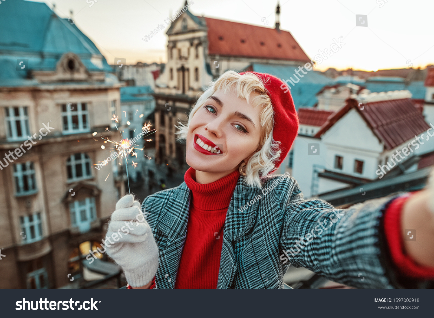 Happy smiling girl with sparkler takes selfie on roof top with beautiful view of old European city. Winter holidays Christmas vacation New Year travel tourism concept. Copy empty space for text