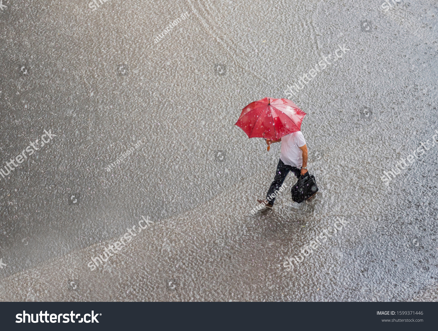 businessman in a very heavy rain walks down the street. is holding bag and red umbrella in hand.