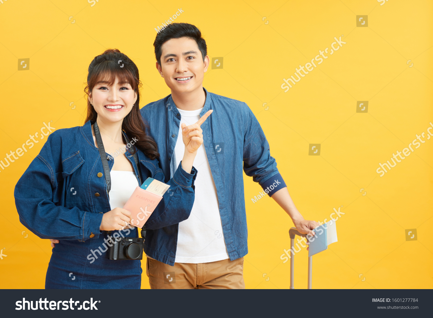 young travelling couple with suitcases pointing somewhere isolated on yellow