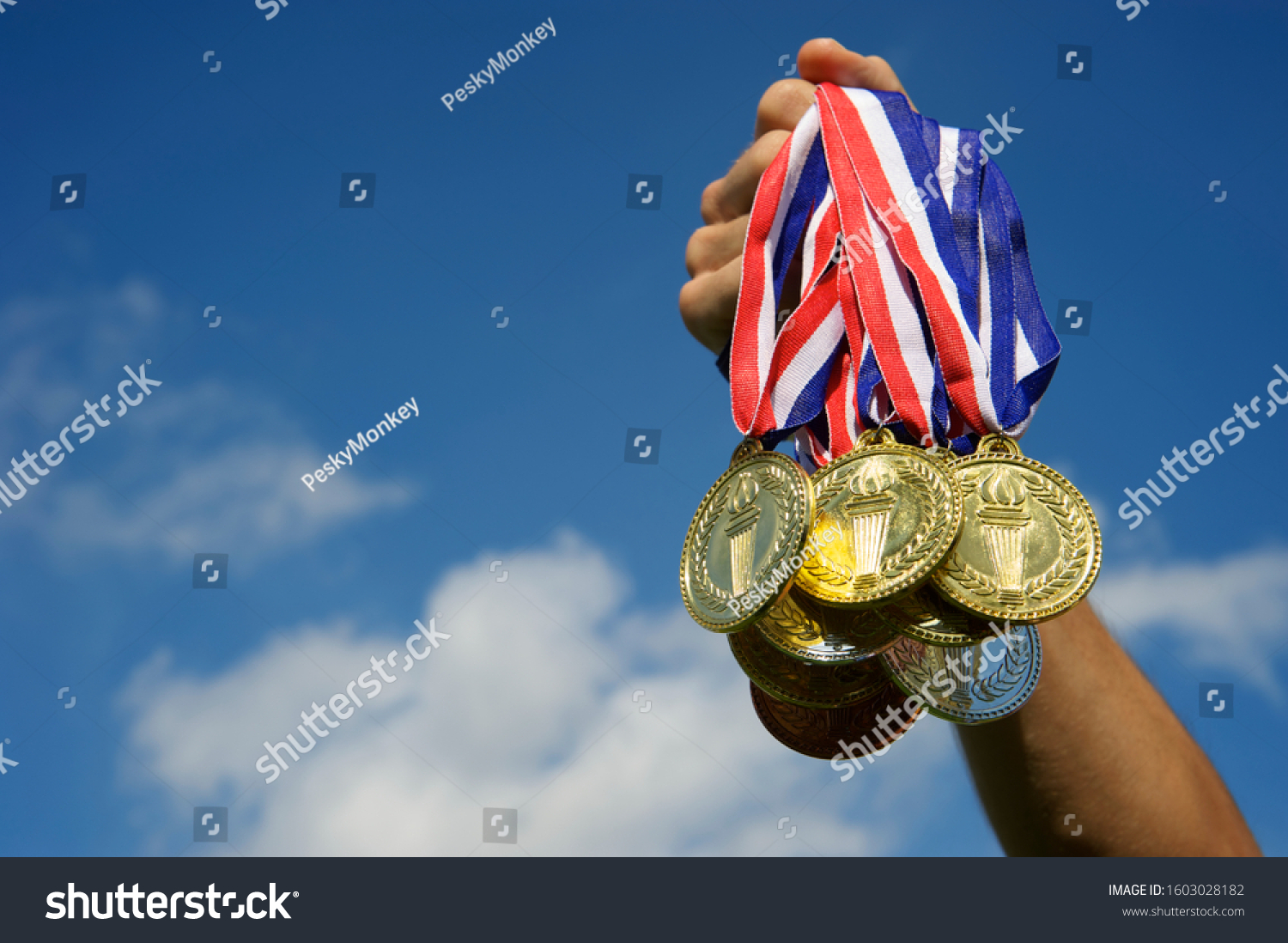 Hand of an unrecognizable athlete holding up a bunch of gold  silver  and bronze medals in bright blue sky