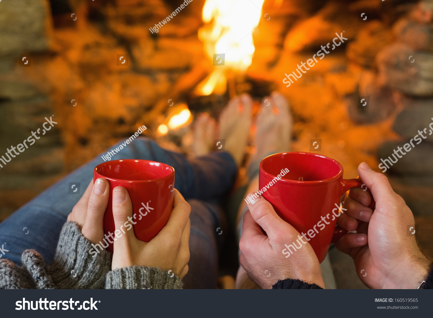 Close-up of hands holding red coffee cups in front of lit fireplace