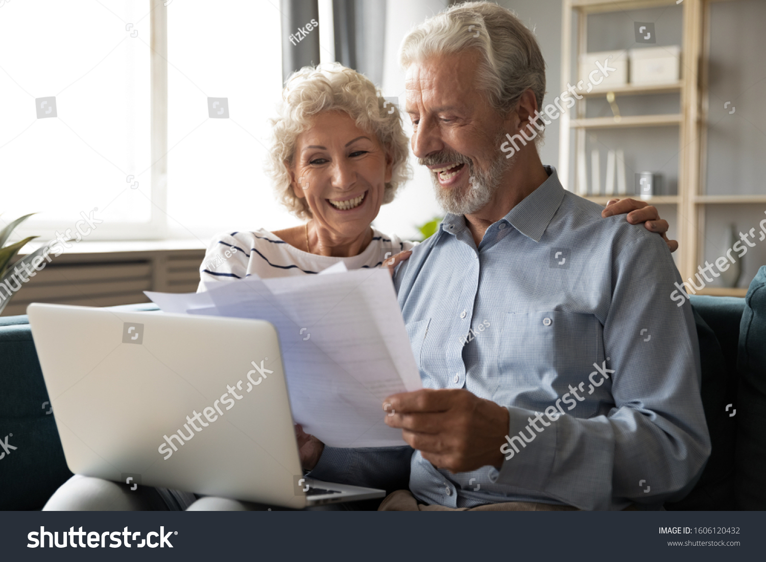 Cheerful elderly grey haired wife and husband sit on couch using