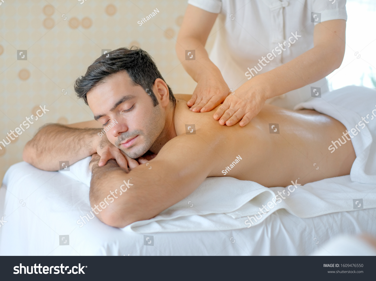 Handsome man enjoy with Thai masseuse massage to him and he lie on bed in spa room with day light.