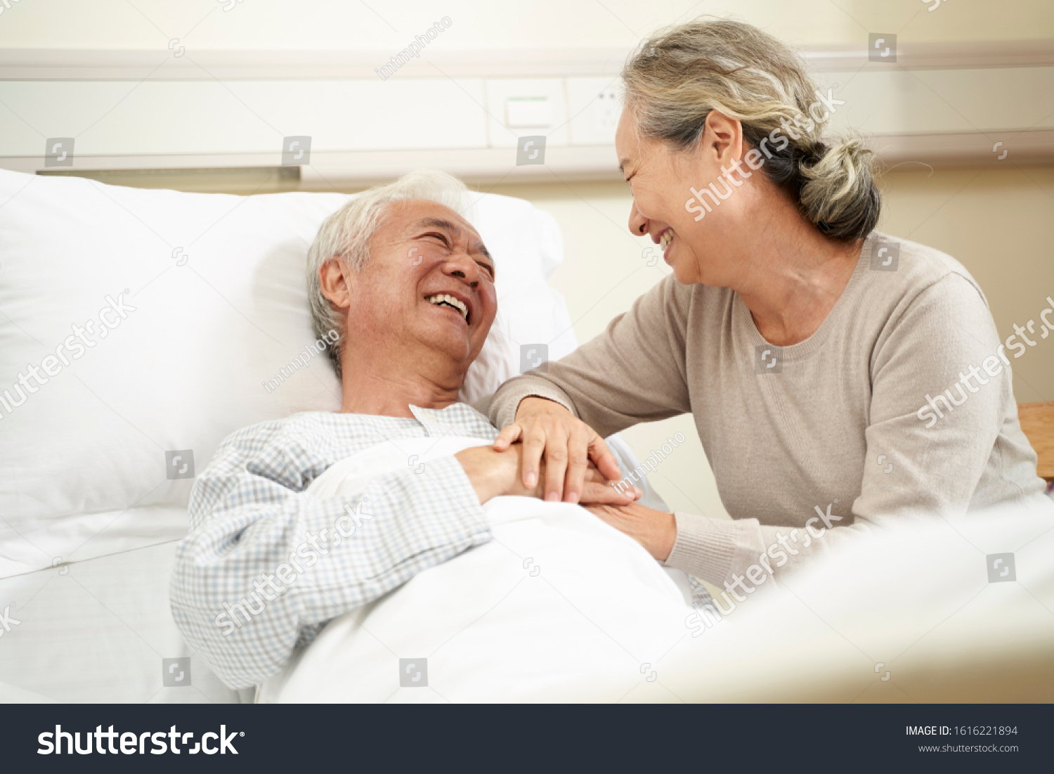 loving and caring senior asian woman visiting and talking to hospitalized husband at bedside