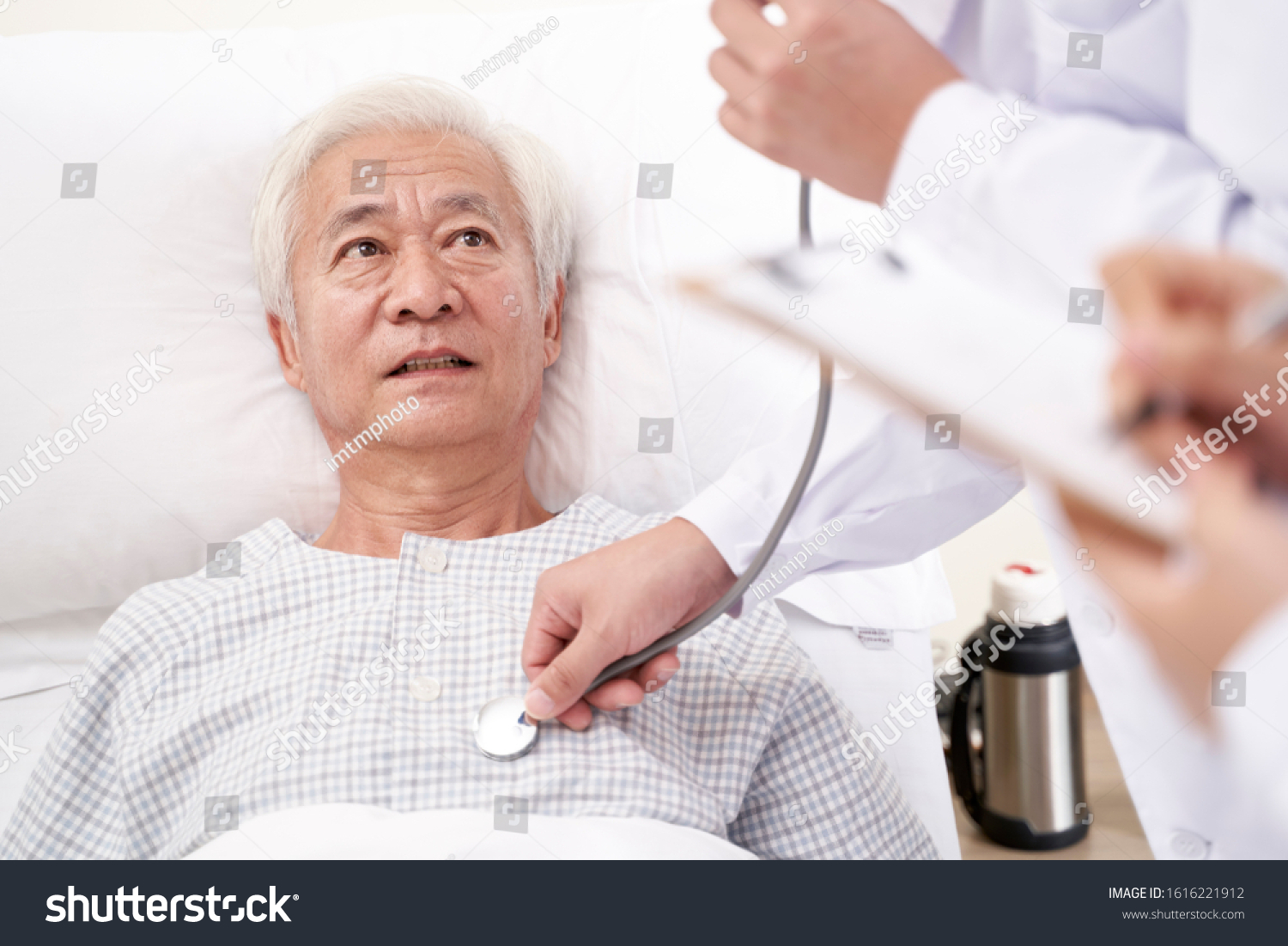 asian old man lying in bed in hospital ward being examined by doctor using stethoscope