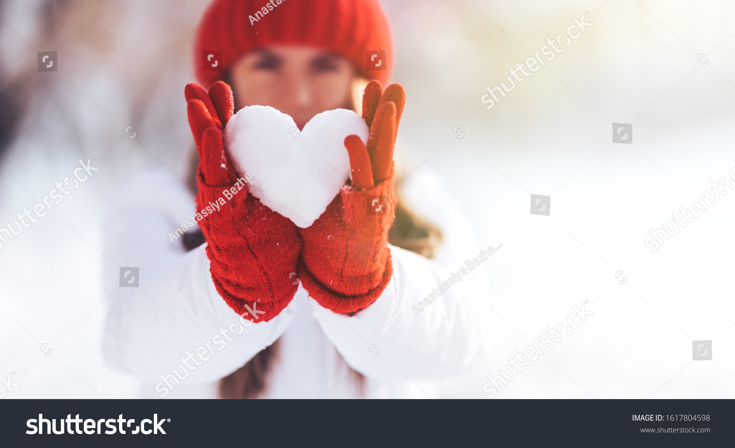 Woman in red gloves and hat holding heart shape from snow Valentines day sun set. love concept.