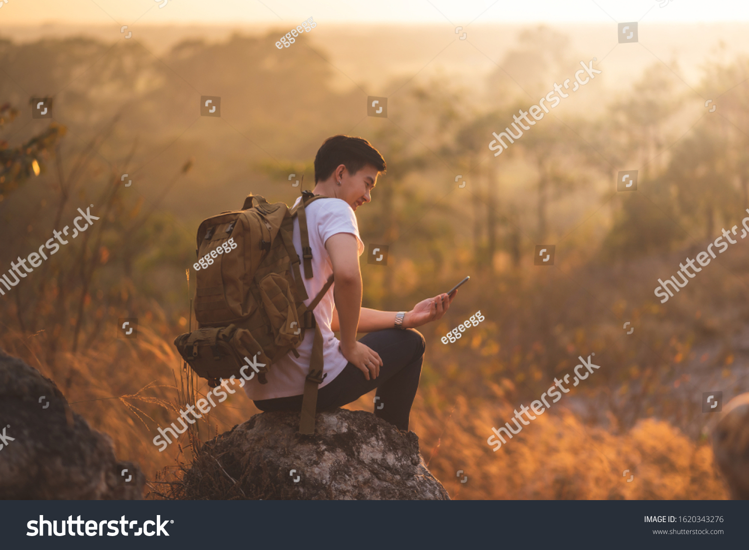 Happy Asian Traveler man is enjoying with beautiful nature sunset during using smartphone. Technology Wireless communication.